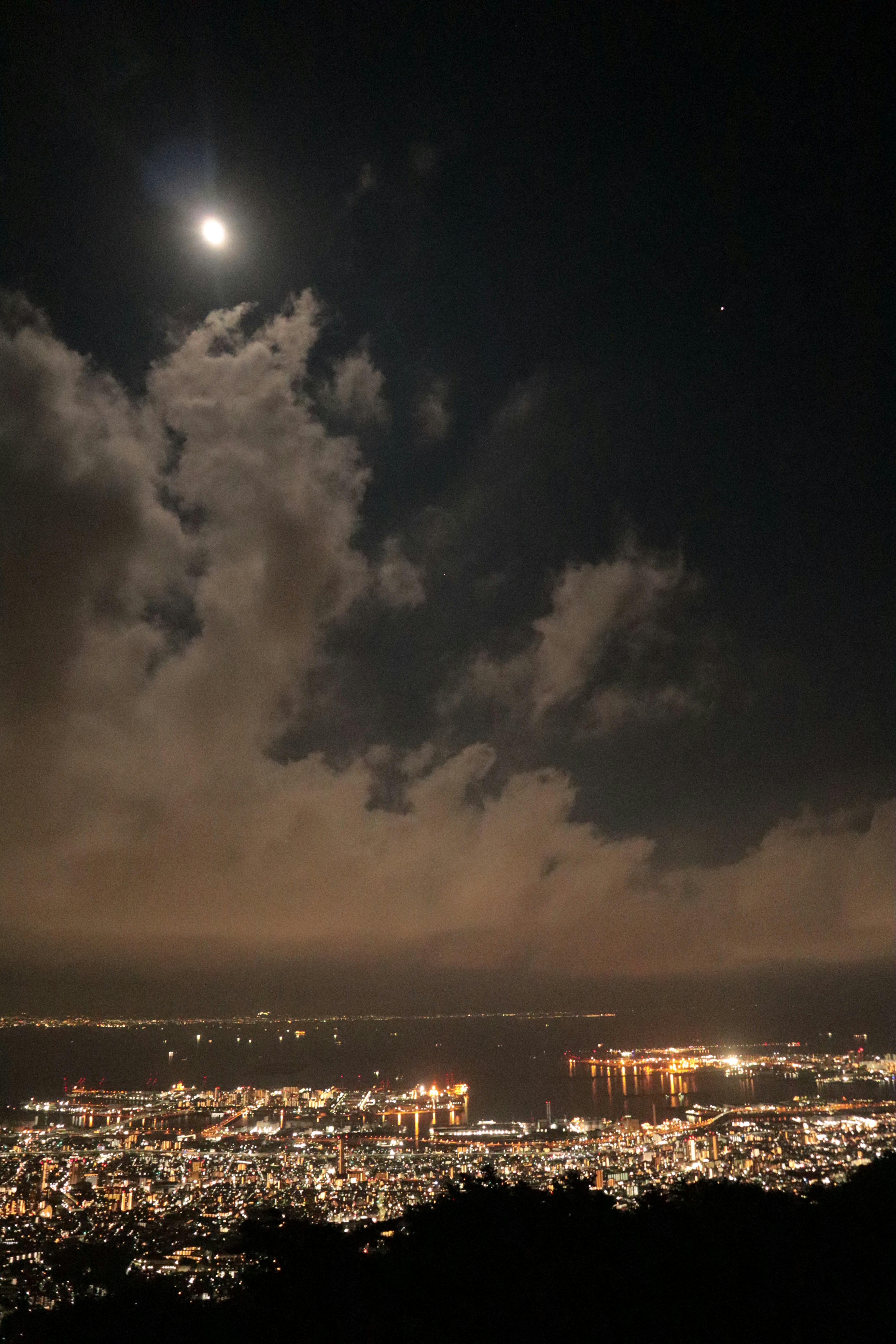 Pemandangan kota malam dengan bulan bersinar dan awan melayang