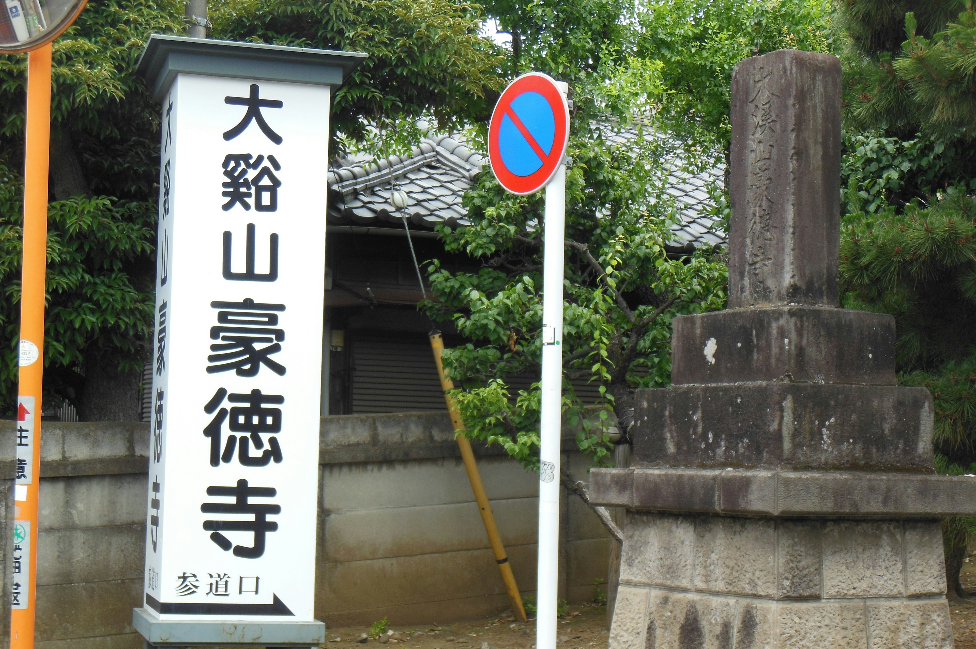 Tanda untuk Daishuzan Gōtoku-ji dengan monumen batu dalam pengaturan hijau