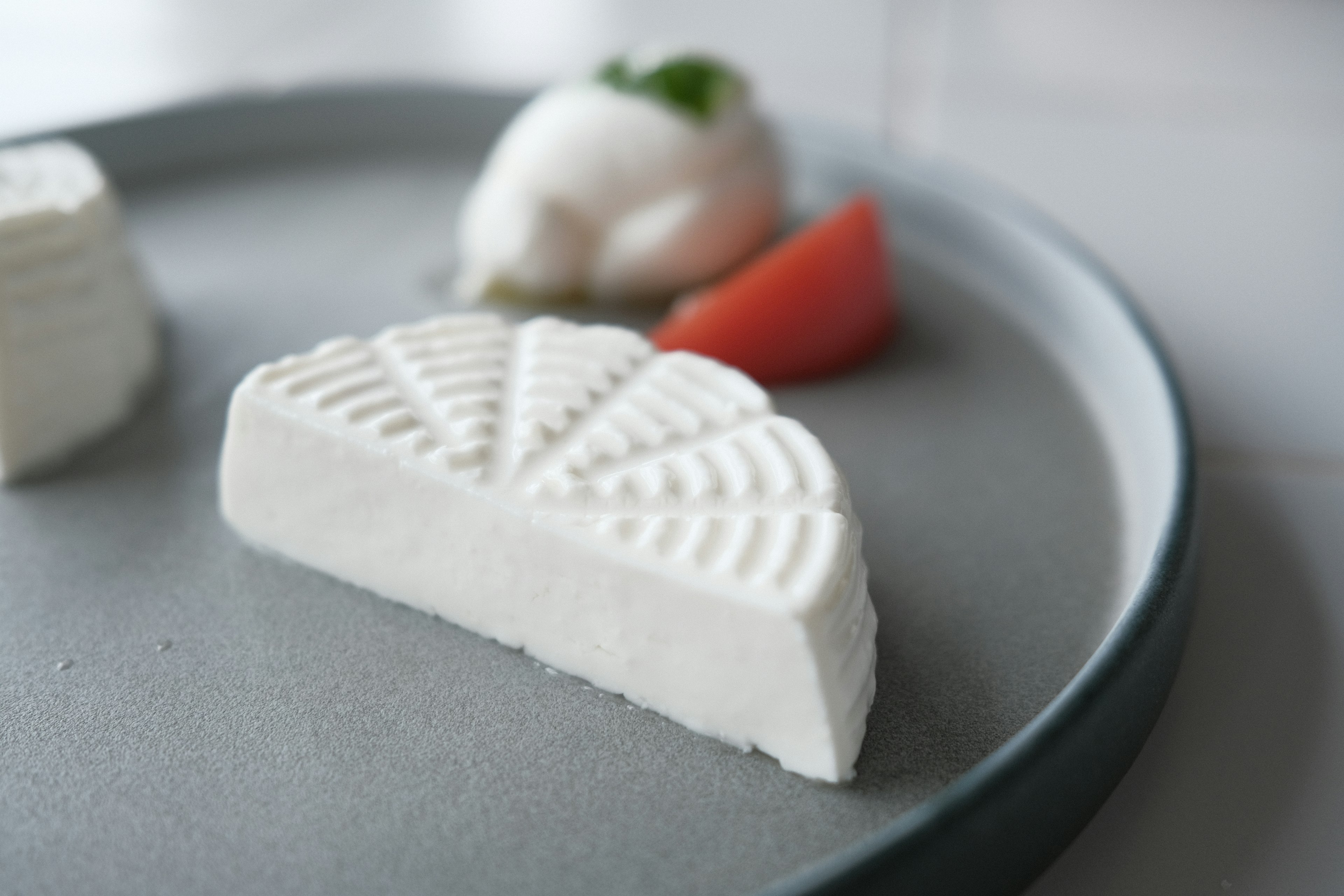 A slice of white cheese on a plate in a fan shape next to a scoop of ice cream and a slice of tomato