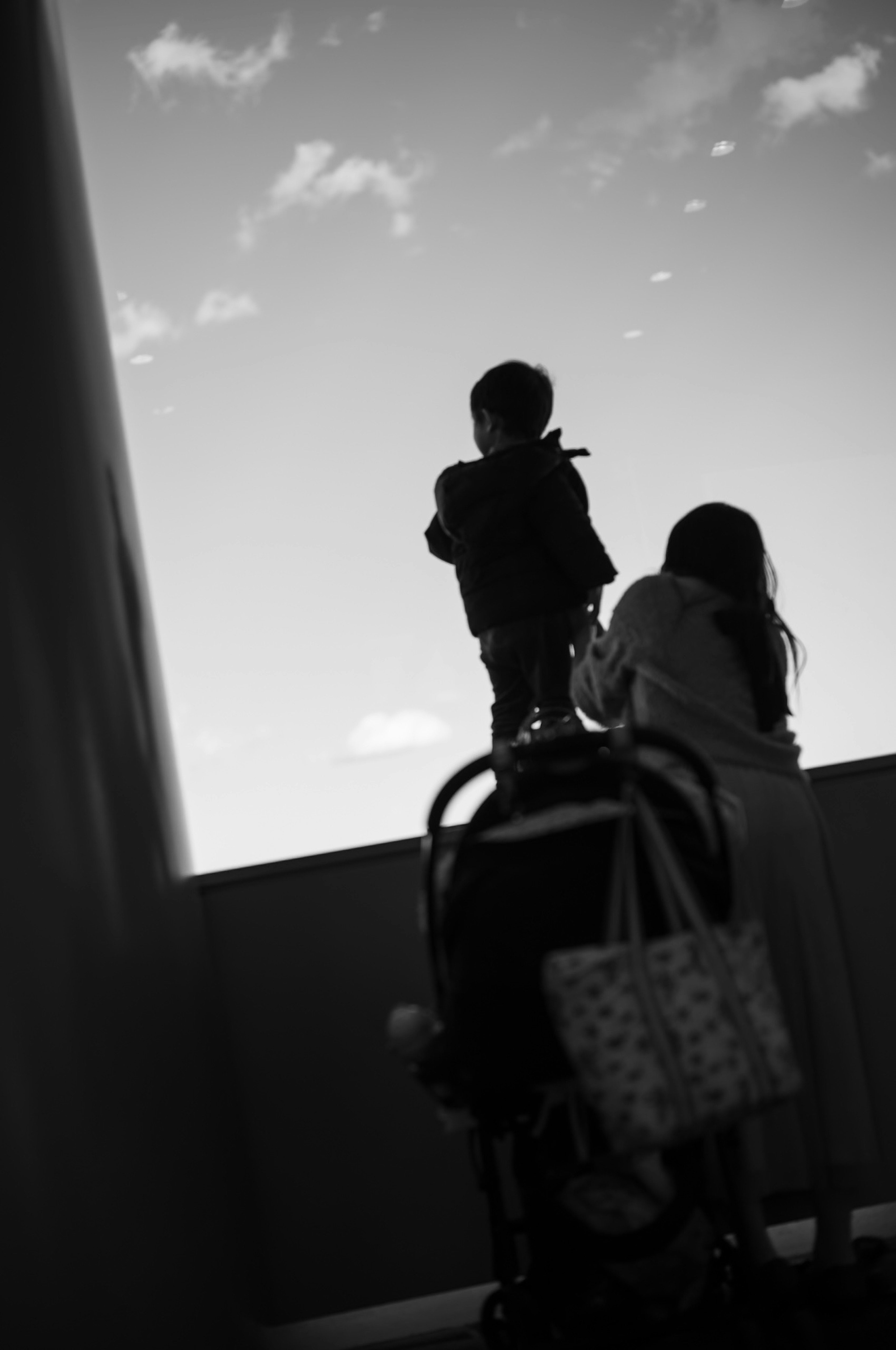 Silhouette of a child looking up at the sky with an adult behind holding a stroller