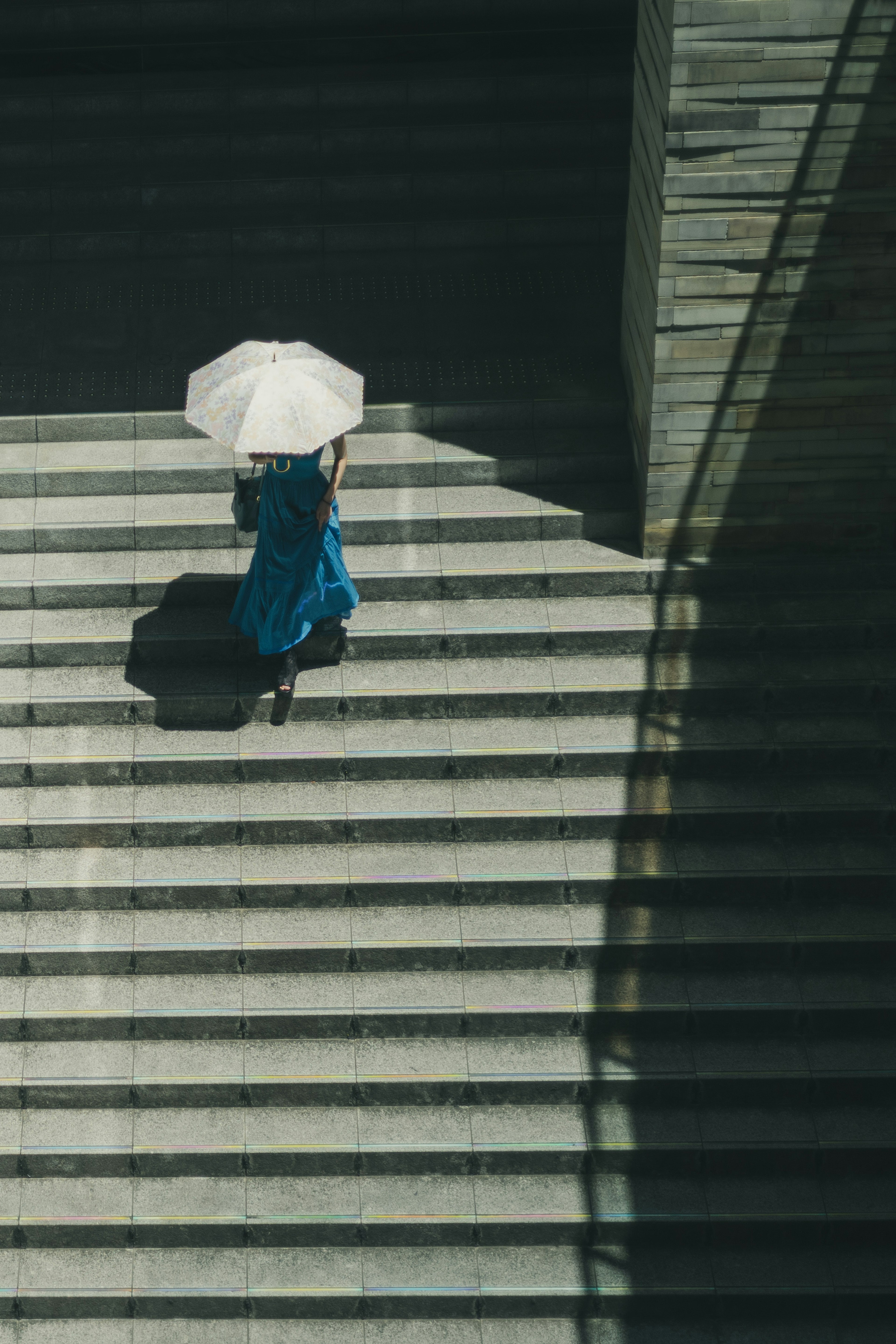 A woman in a blue dress holding a white umbrella walking down stairs