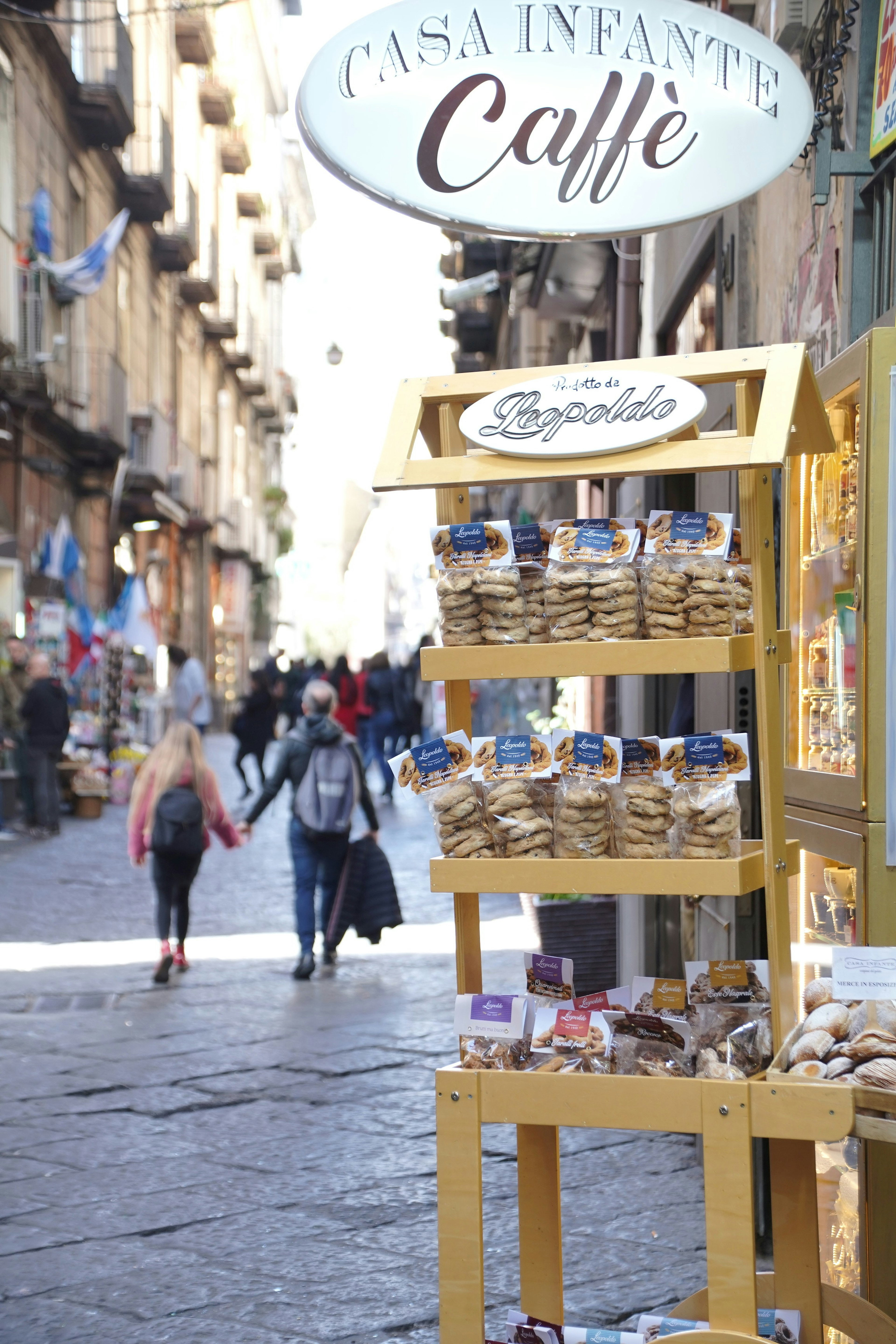 Yellow stand with pastries in front of a café and people walking in the street