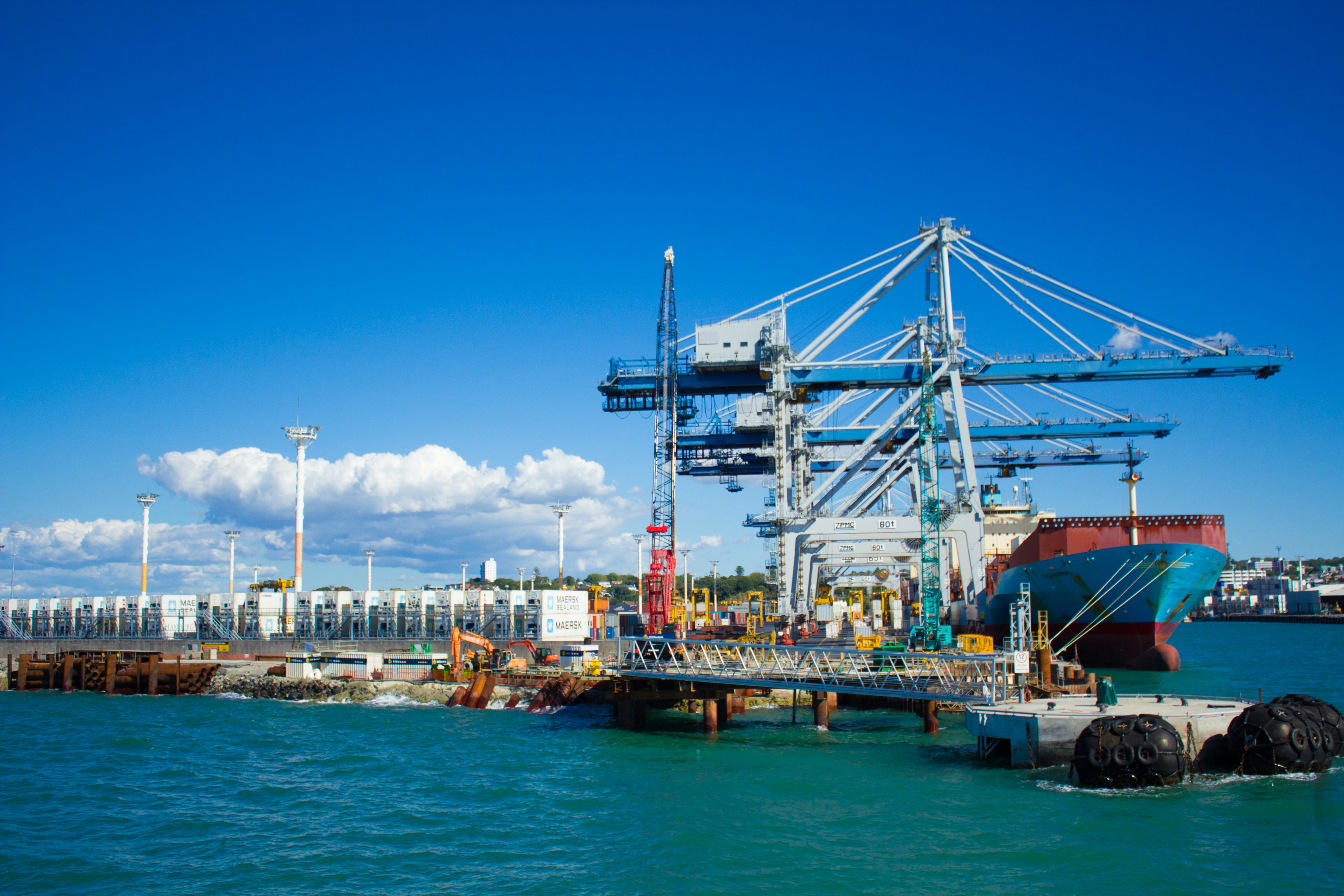 Une scène de port vibrante avec des grues et un navire sous un ciel bleu clair