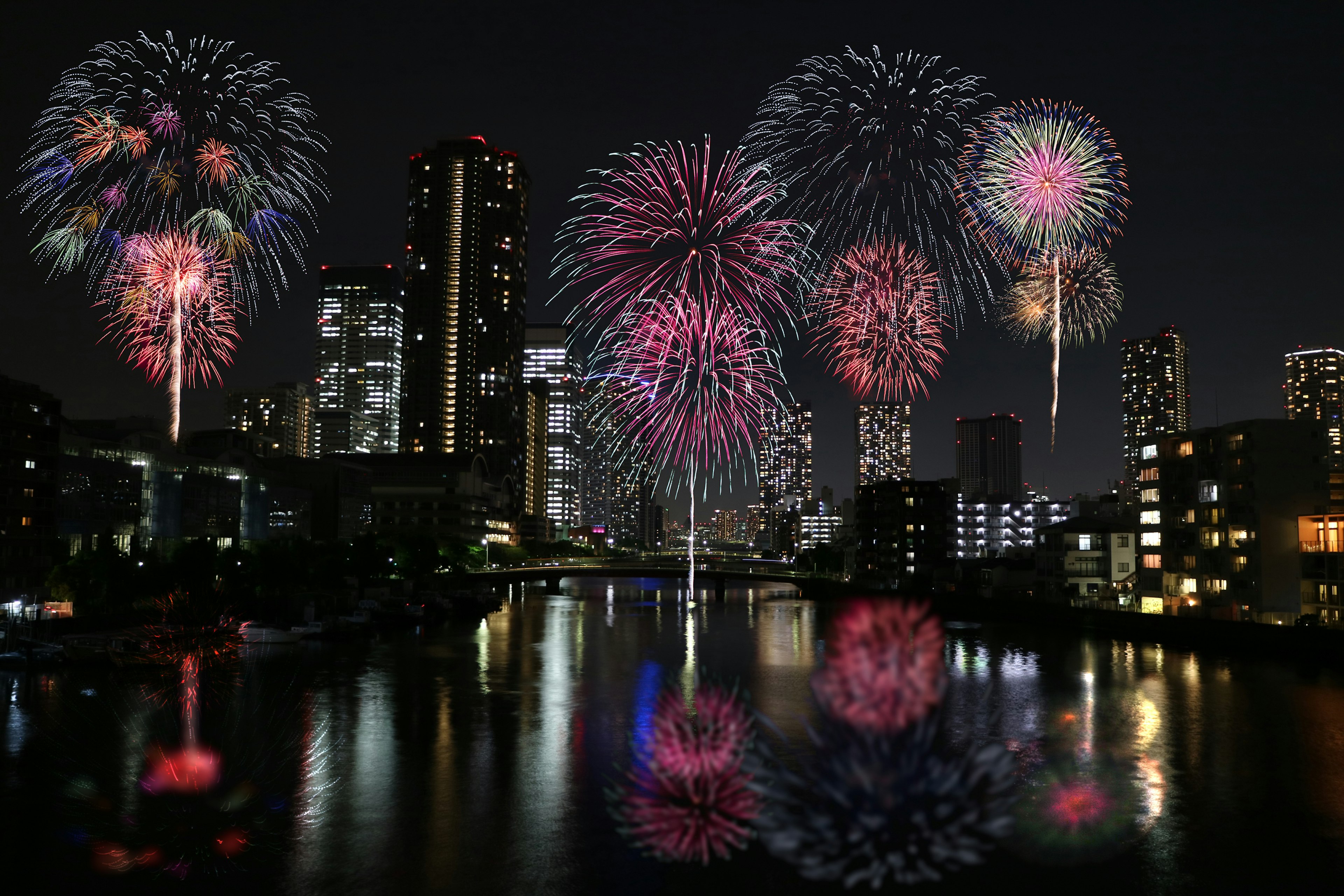 夜空中五彩缤纷的烟花在城市天际线上方倒映在水中