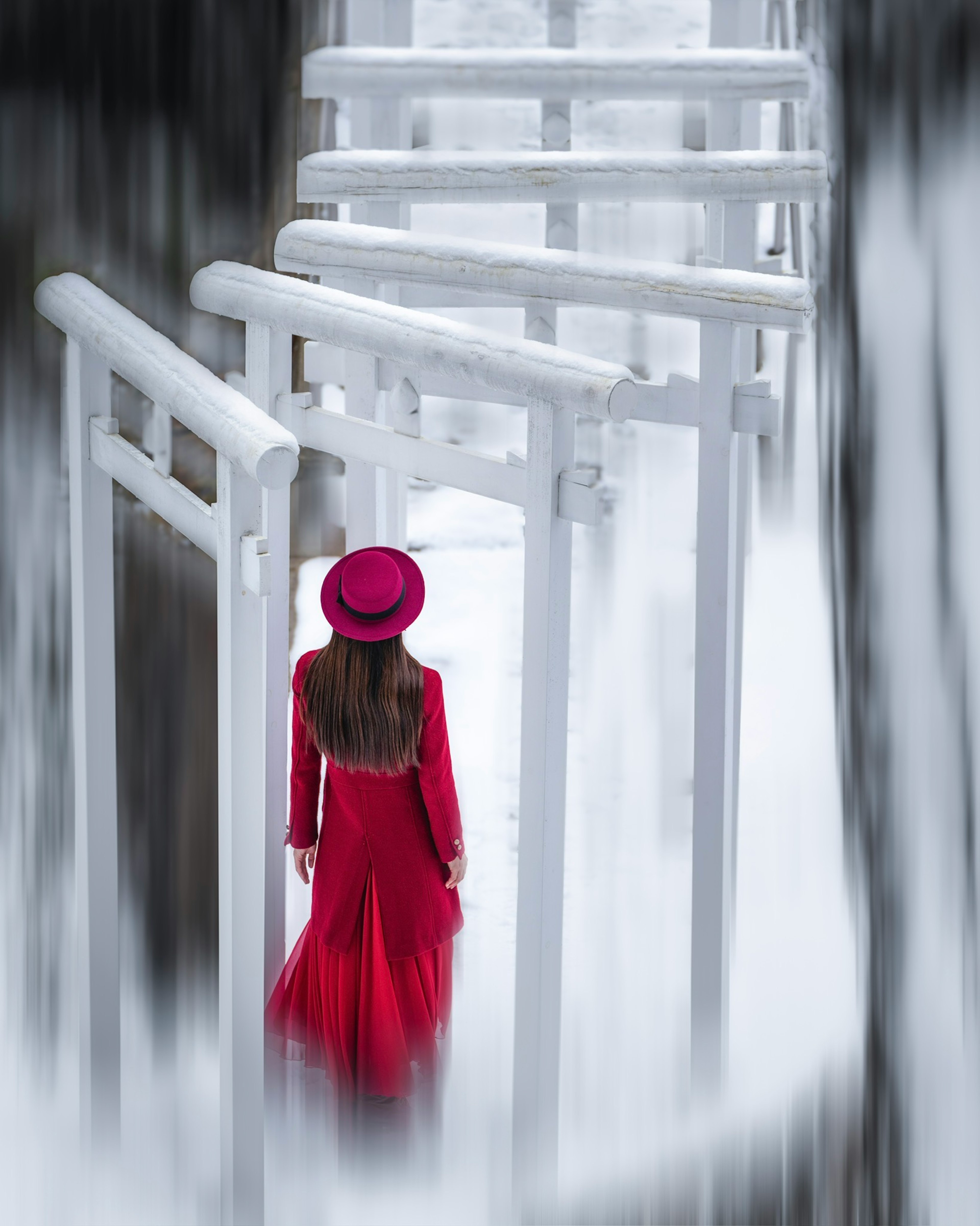 Una donna in abito rosso che cammina attraverso porte torii bianche in un ambiente nebbioso