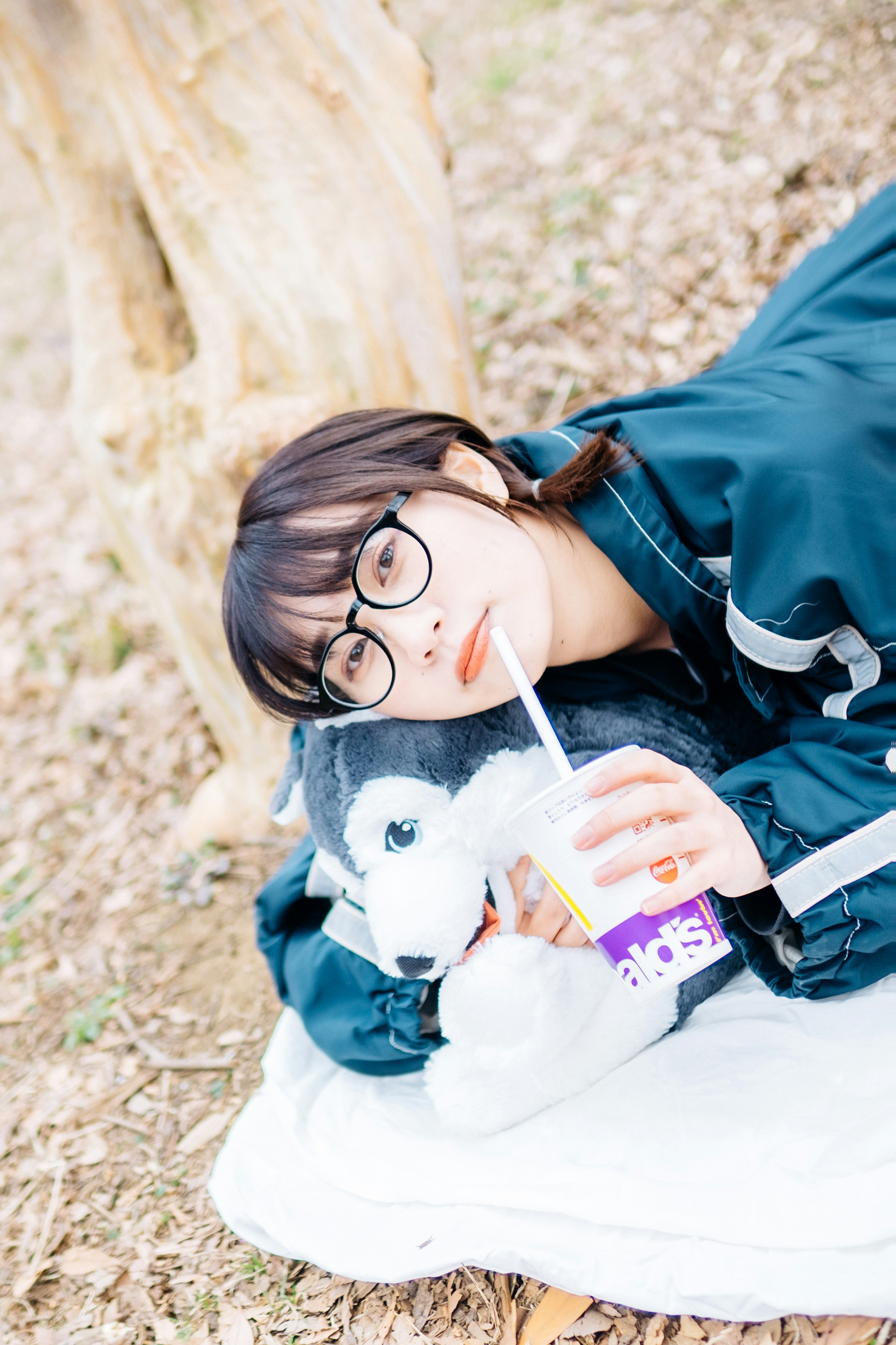 Woman lying under a tree holding a stuffed animal and a drink