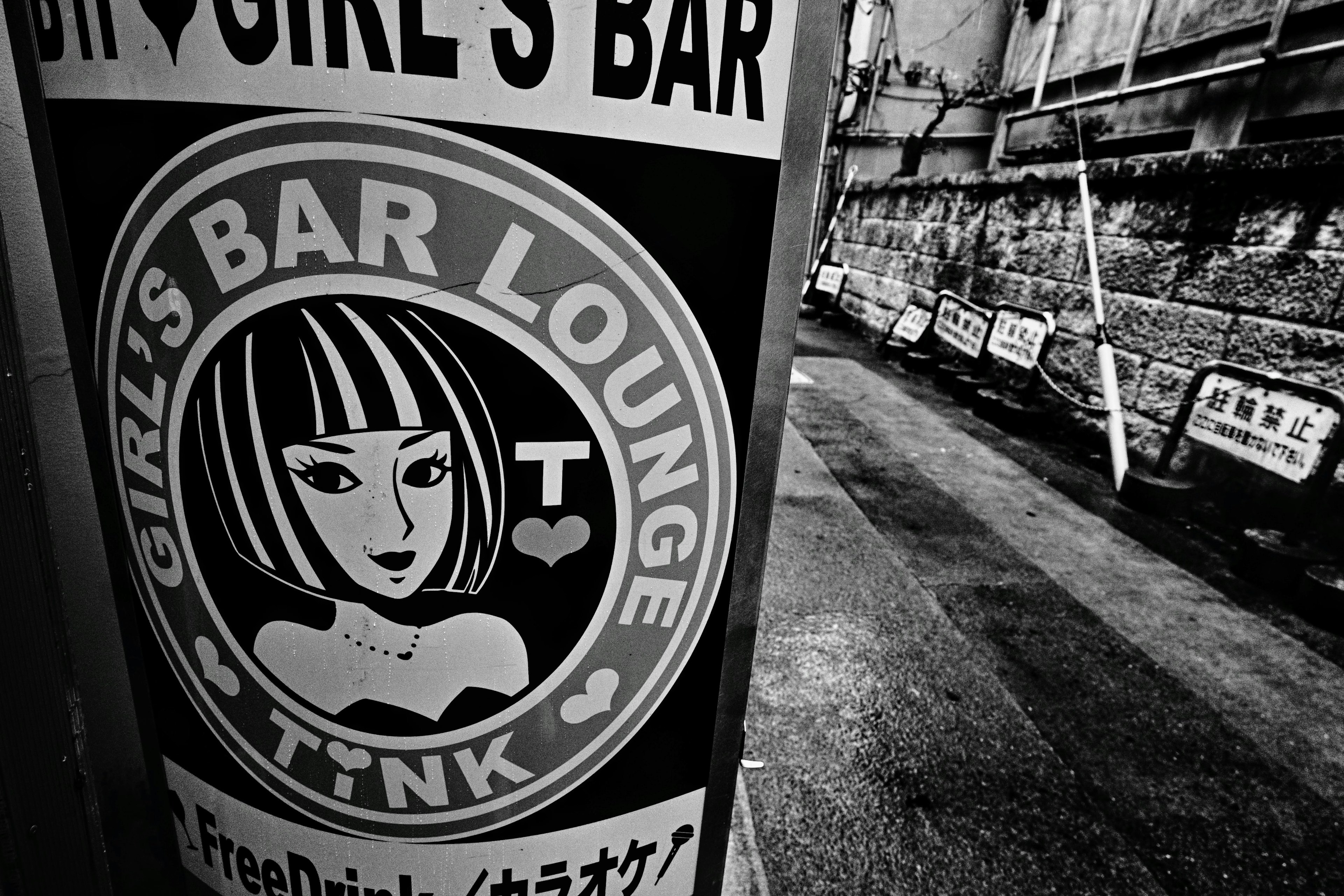 モノクロの看板に描かれたスタイリッシュな女性のイラストと「GIRL'S BAR LOUNGE TINK」の文字