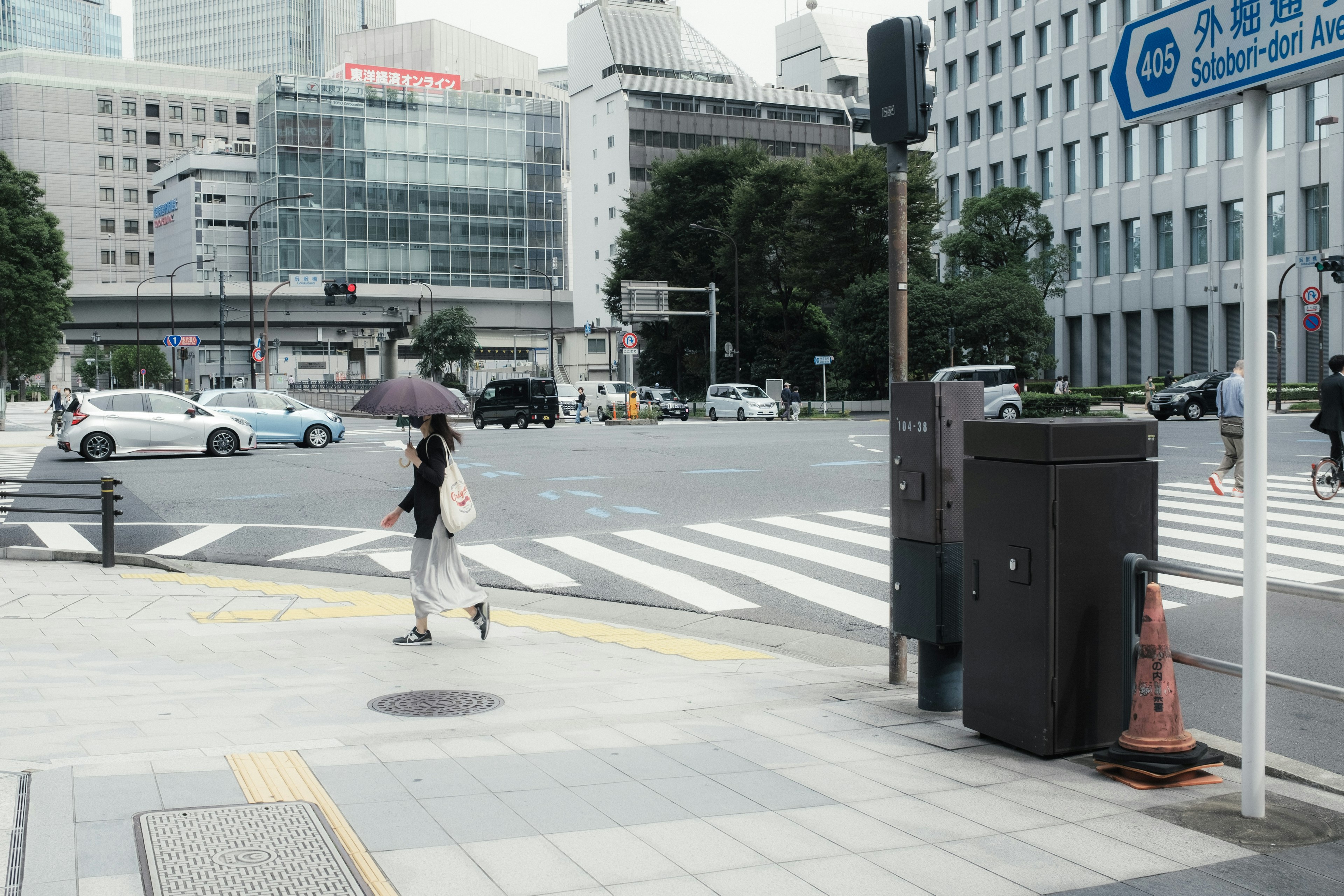 都市の交差点で傘を持つ女性が歩いている風景