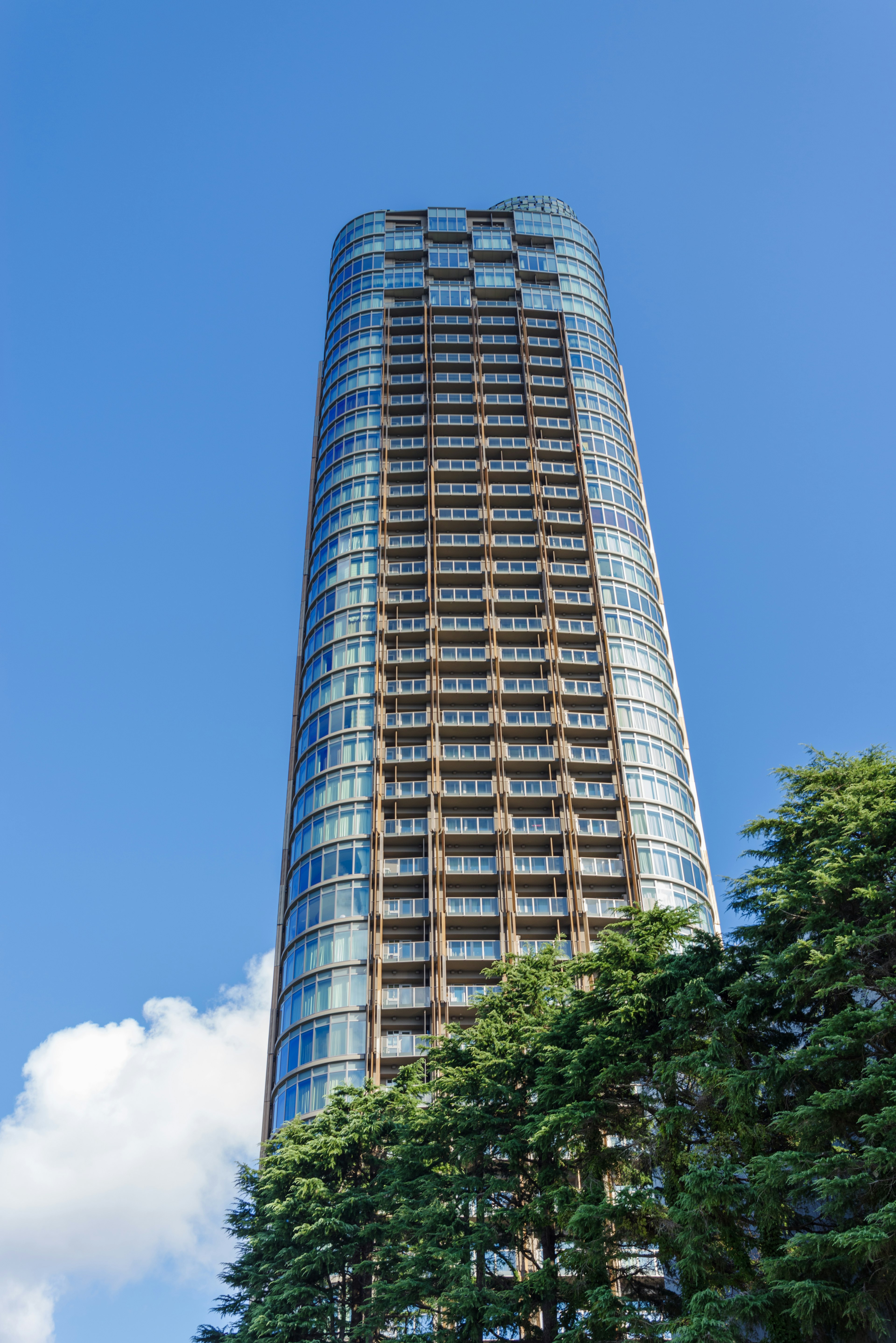 Tall skyscraper against a clear blue sky with green trees