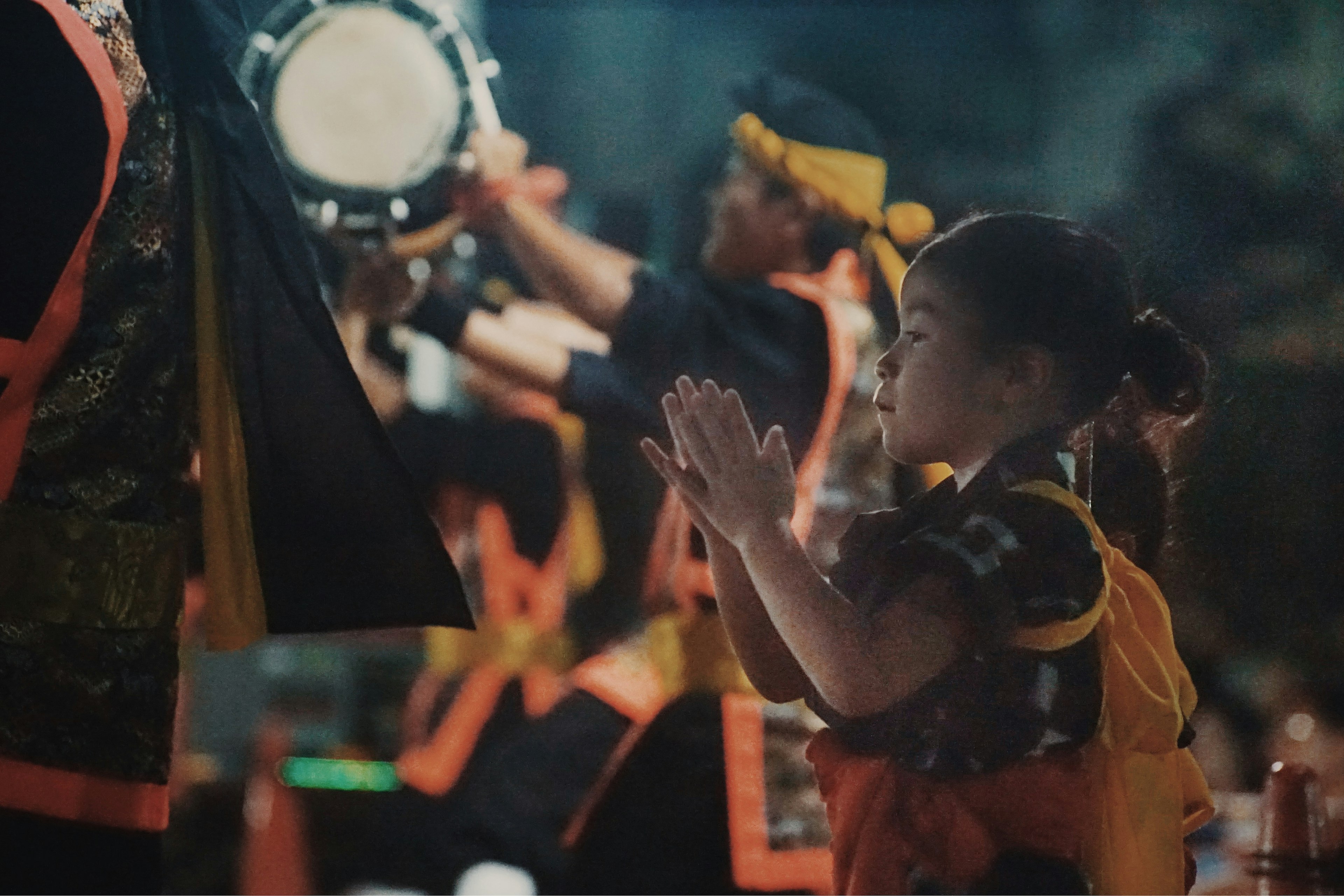 Una niña con atuendo de festival rezando frente a los percusionistas