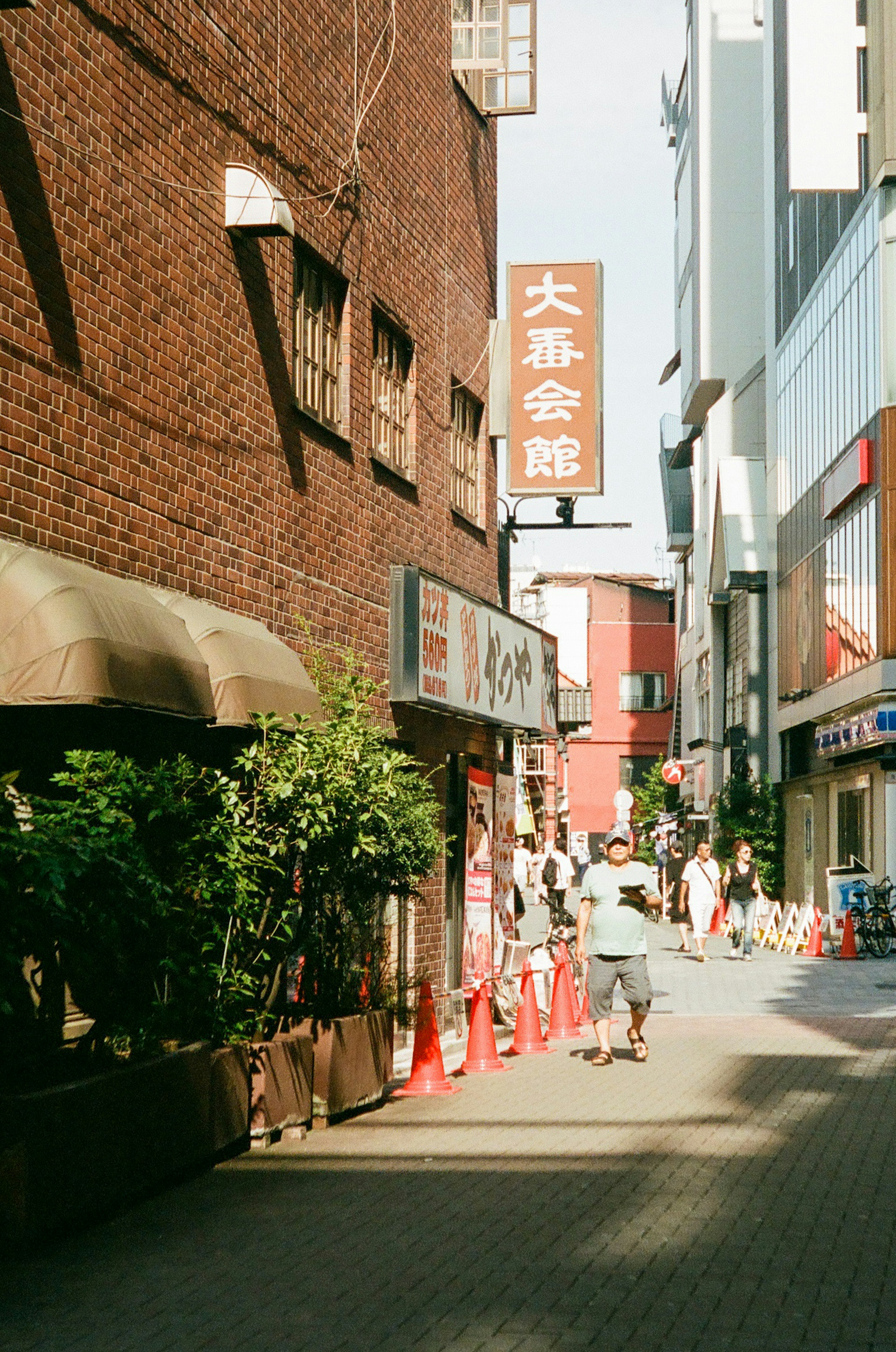 Street view featuring red brick buildings a café with plants and a prominent sign