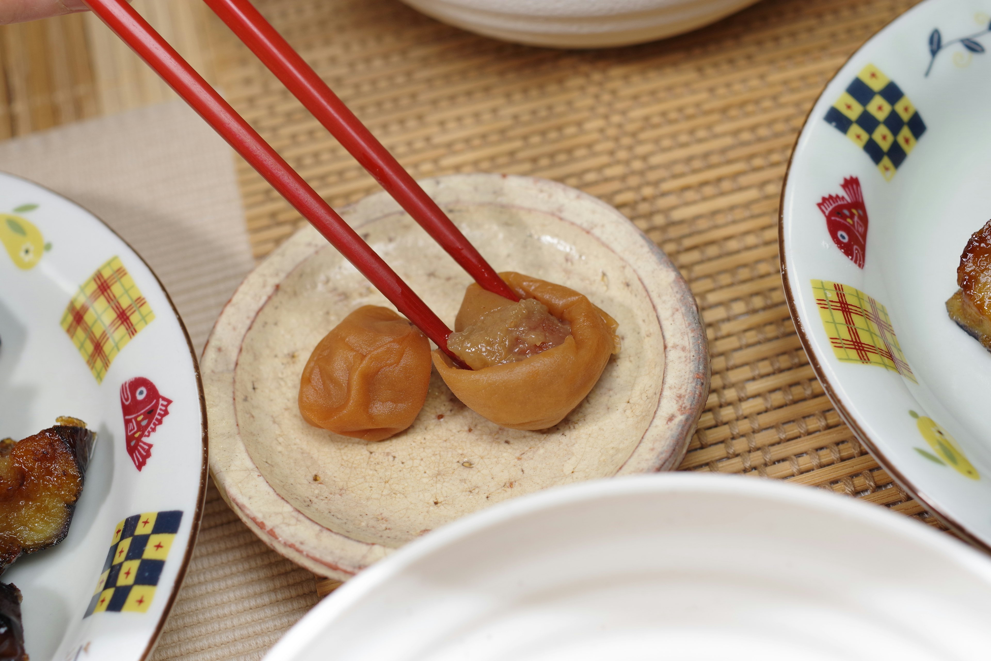 Pickled plums being picked up with chopsticks on a small plate