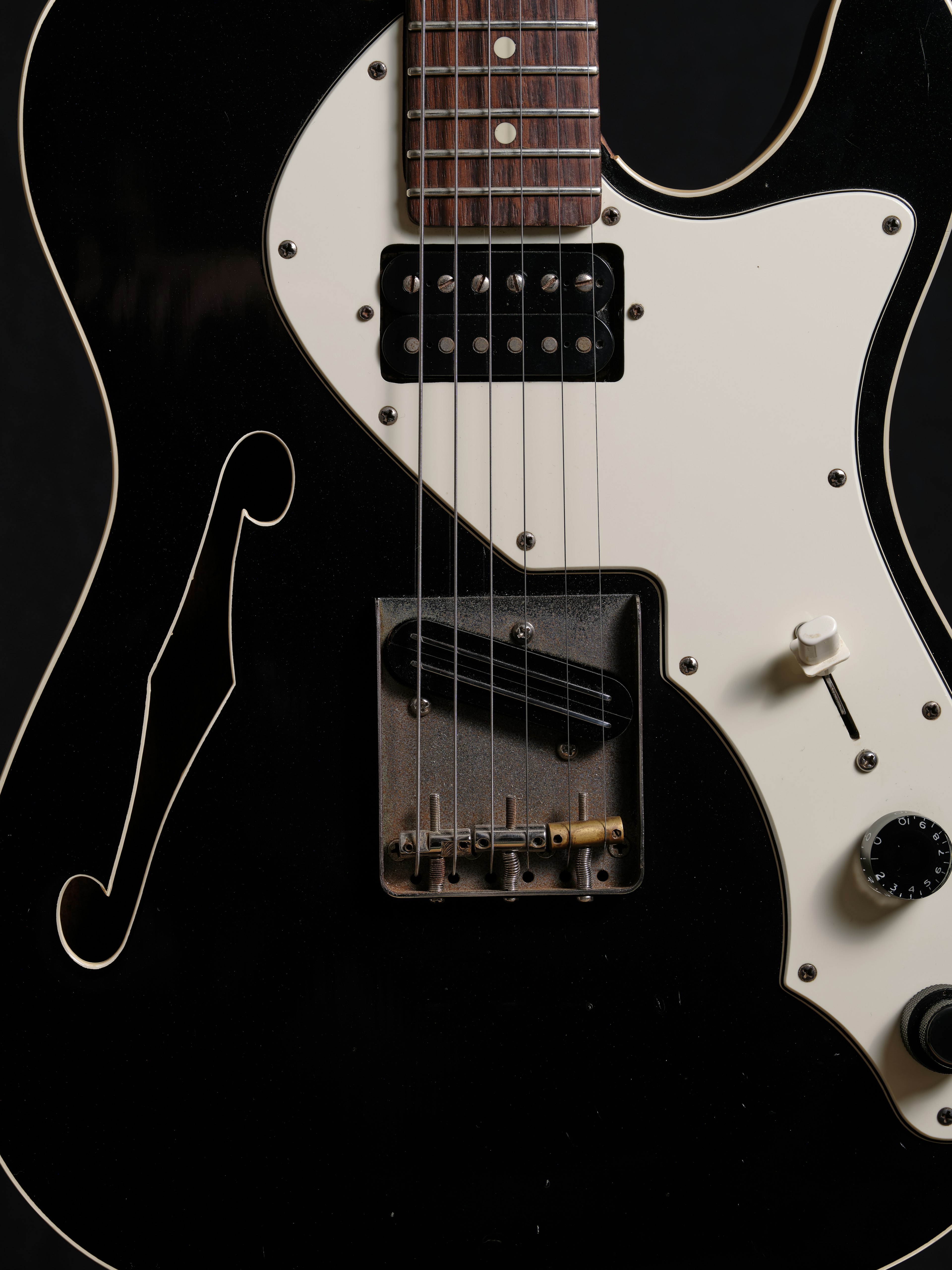 Close-up of a black electric guitar featuring a white pickguard and string details