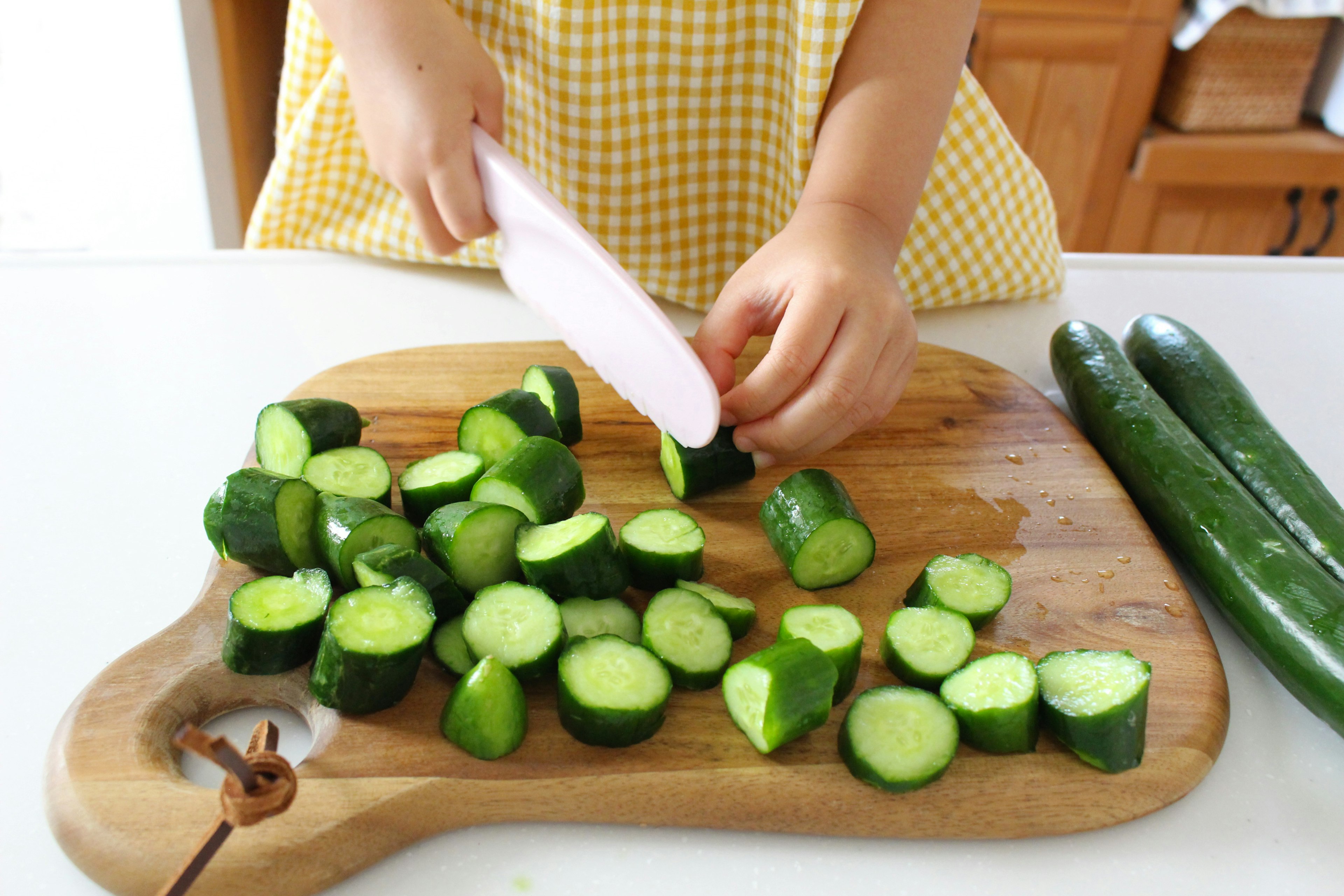 Child's hands chopping cucumbers on a wooden cutting board