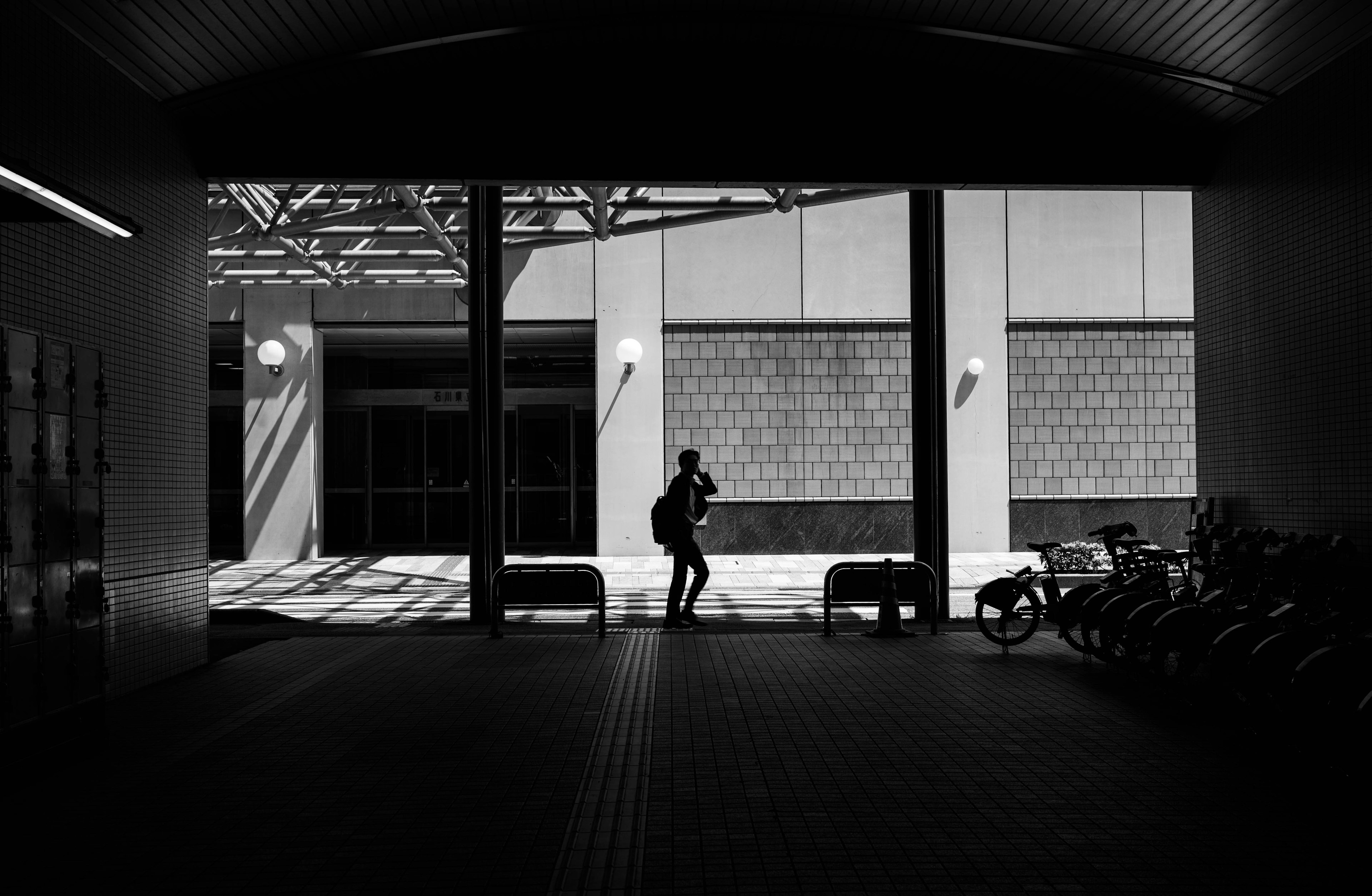 Silhouette di una persona che cammina attraverso un passaggio urbano in bianco e nero