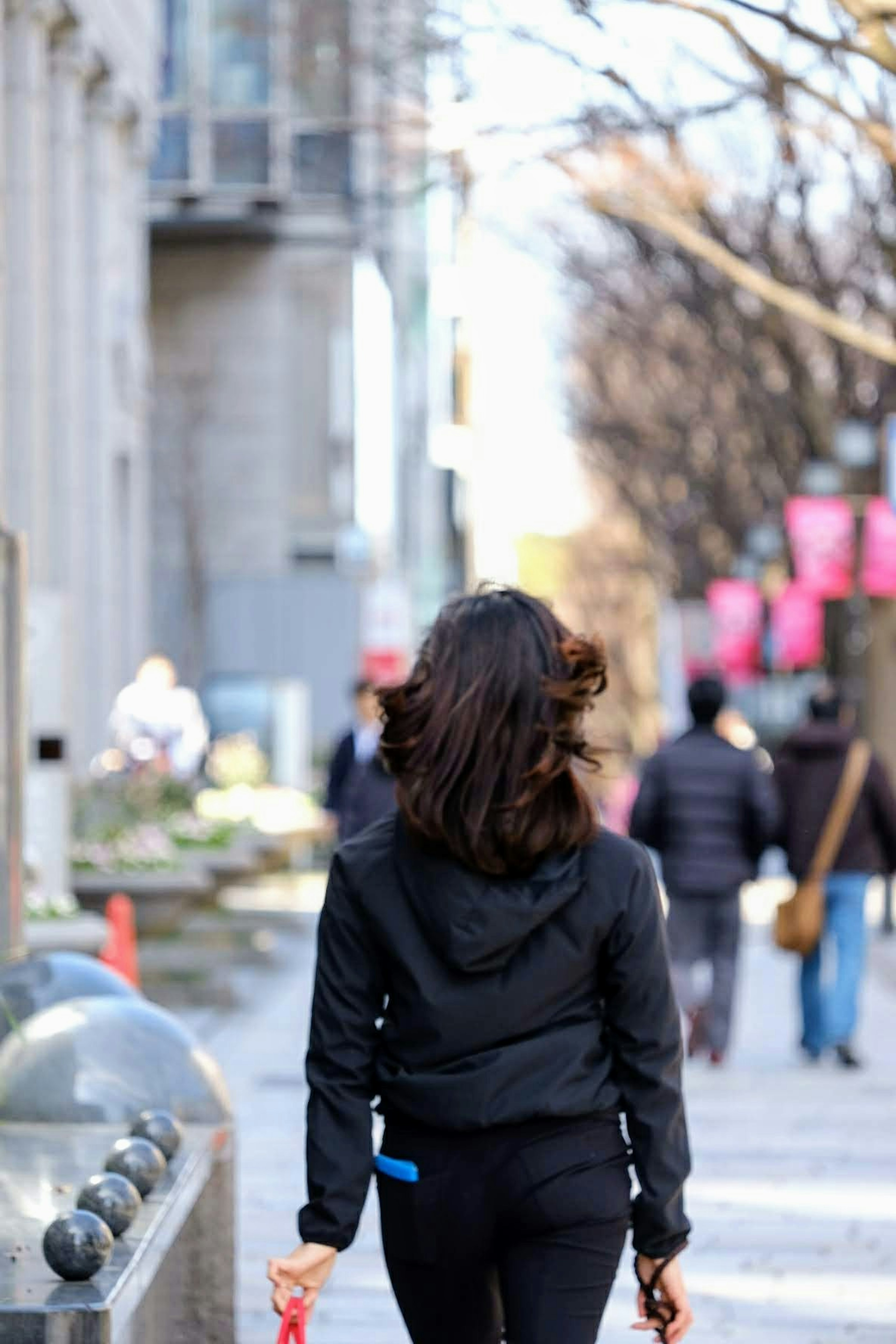 Frau in schwarzer Jacke, die eine Stadtstraße entlanggeht