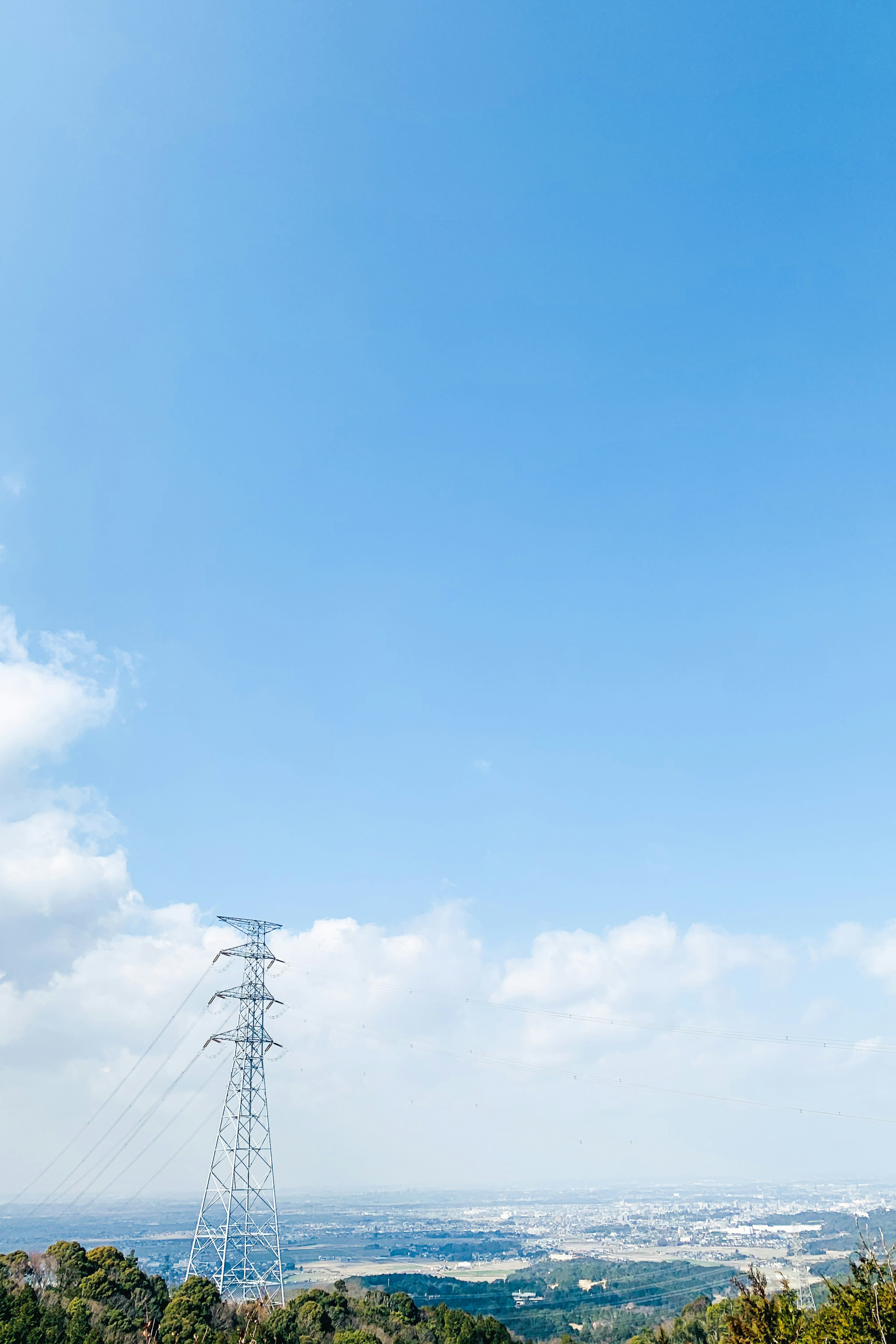 青空と白い雲の下に立つ高圧電線の塔と広がる風景