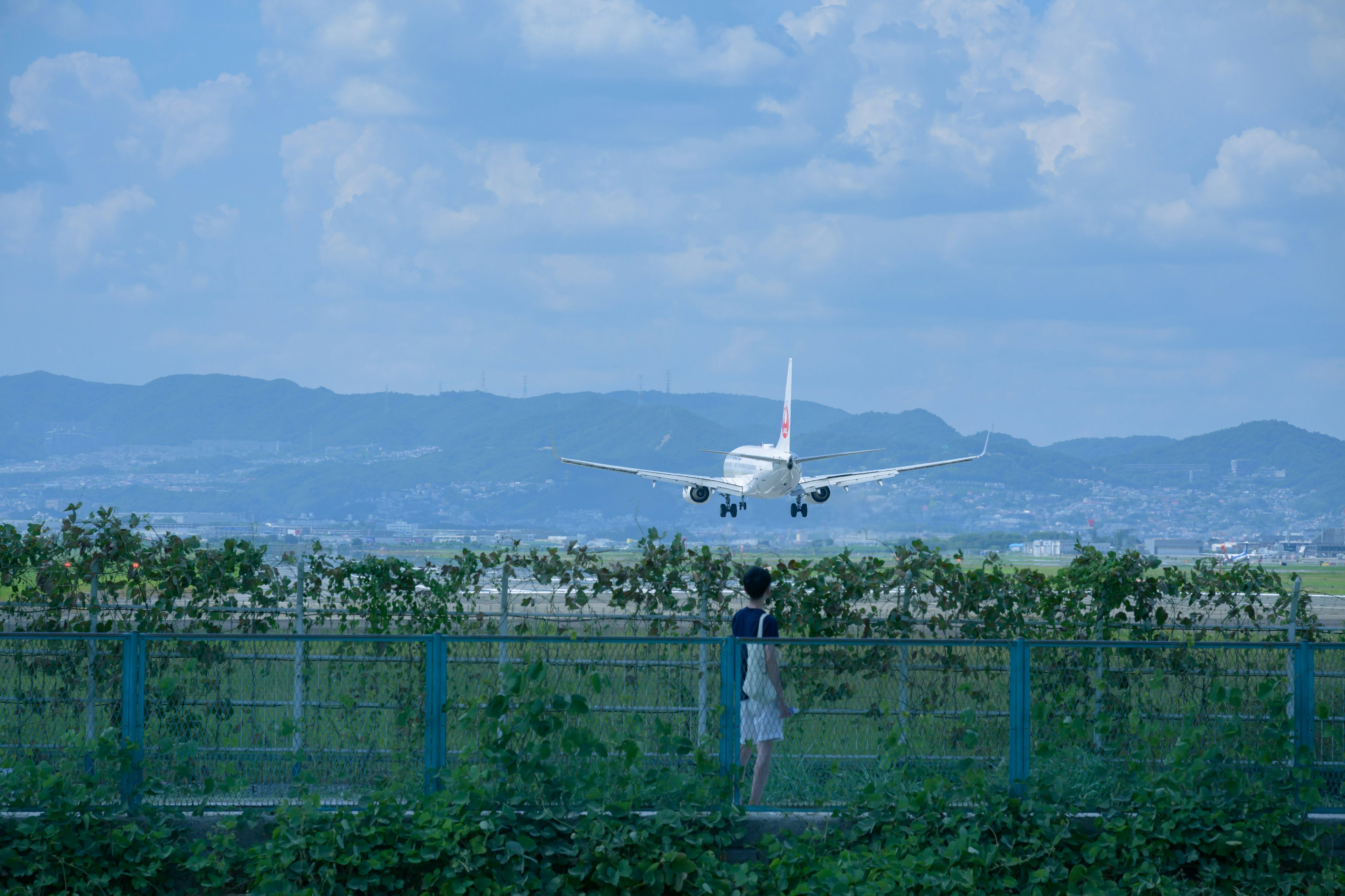 Una persona observando un avión aterrizar bajo un cielo azul con montañas de fondo