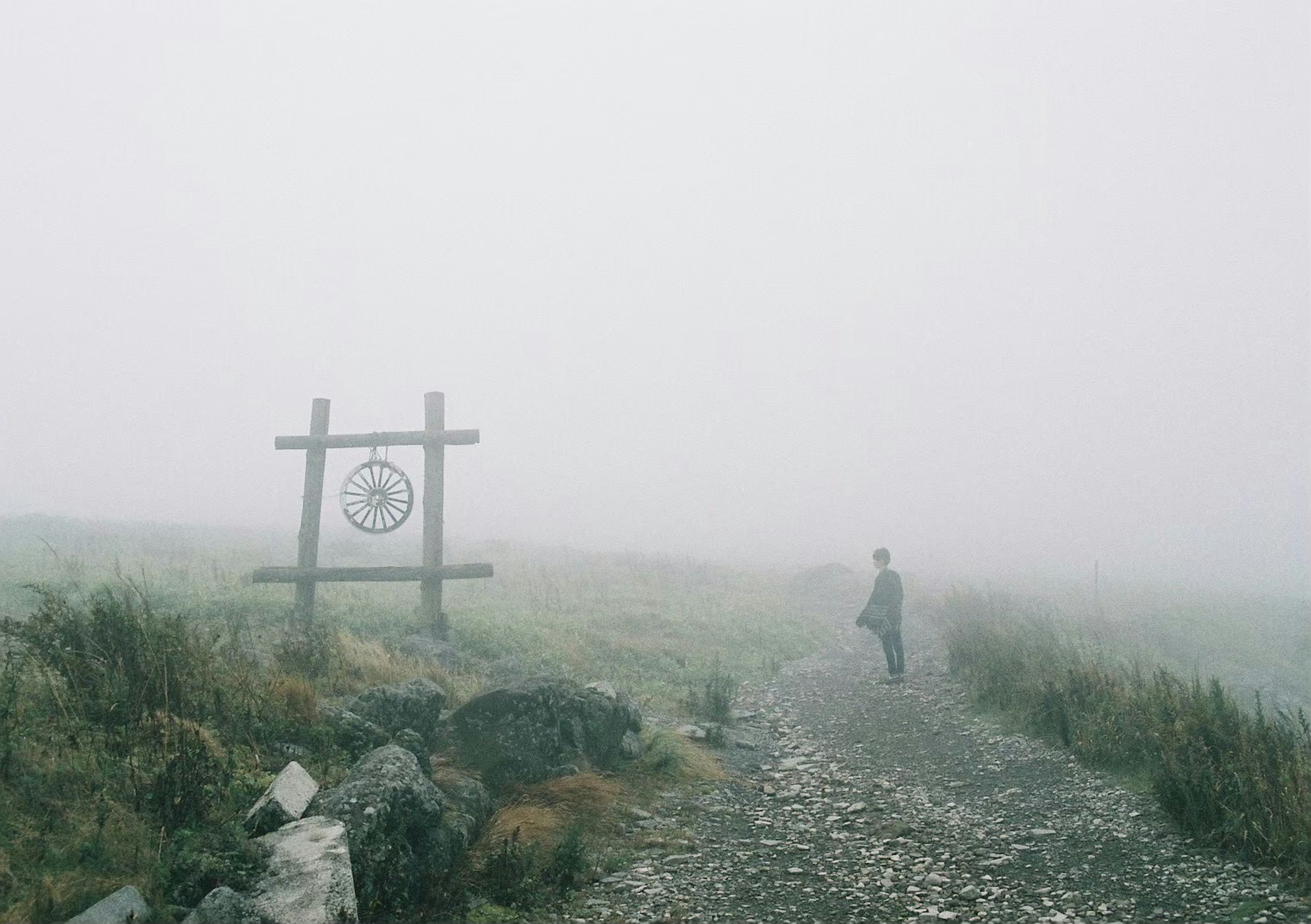 A person walking on a rocky path in a foggy landscape with a signpost