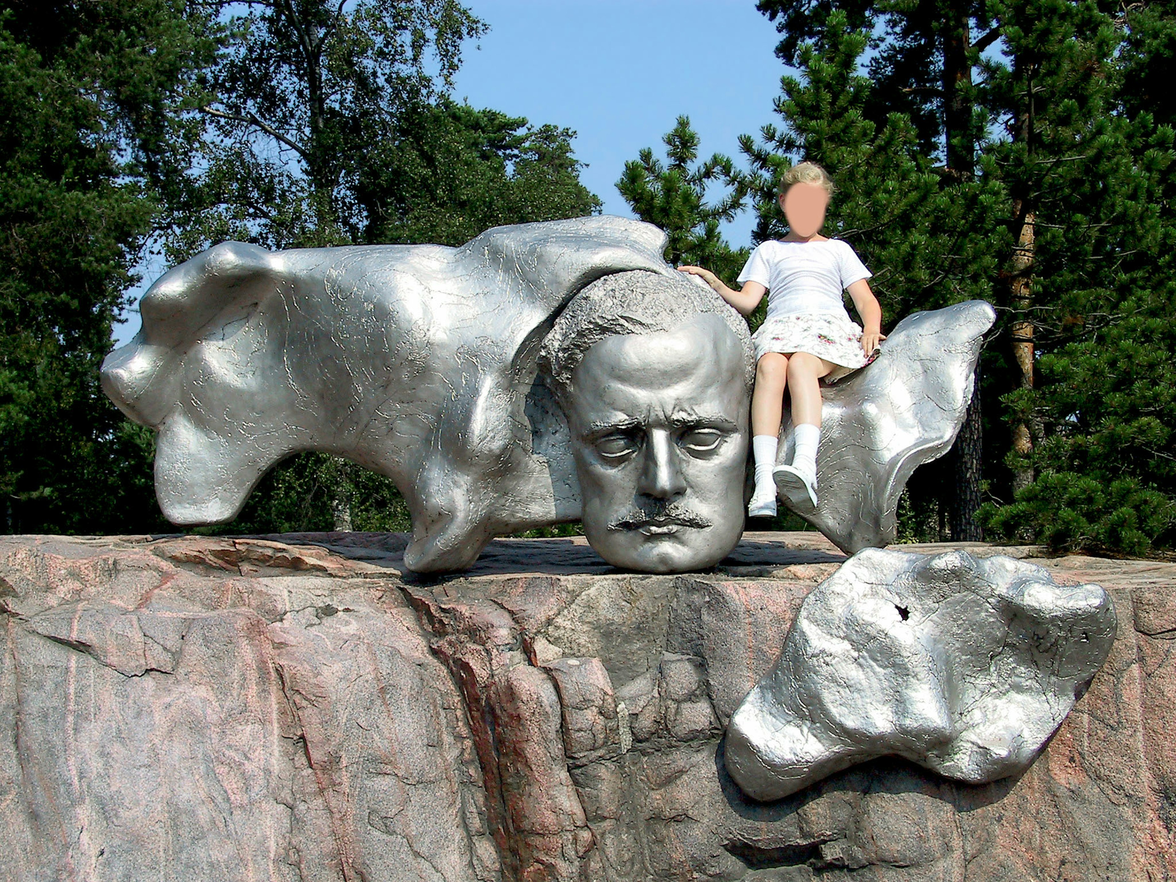 Scultura argentata con una testa e una bambola seduta su una roccia