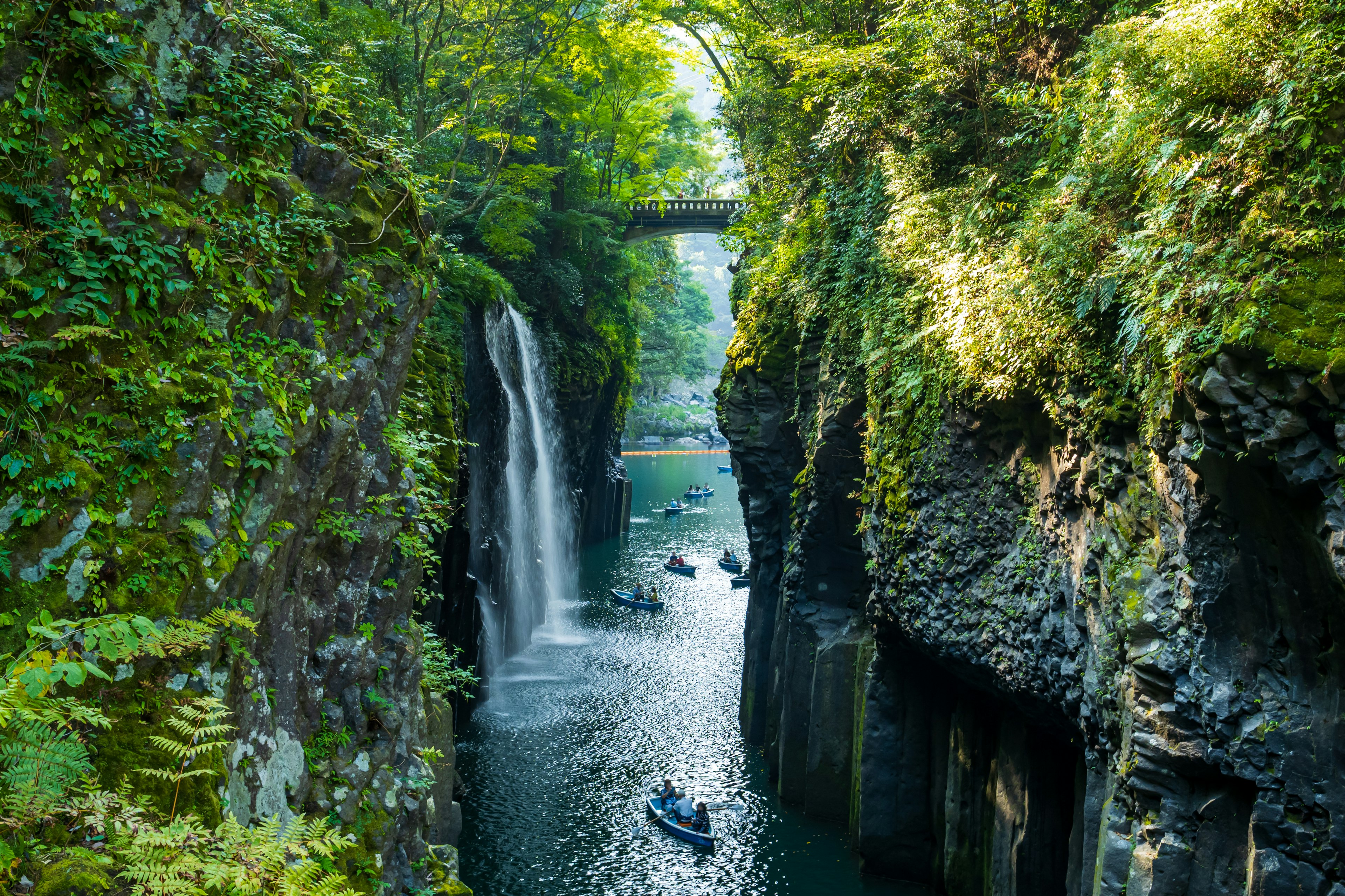 Canyon mit einem Wasserfall umgeben von Grün und Booten auf dem ruhigen Wasser