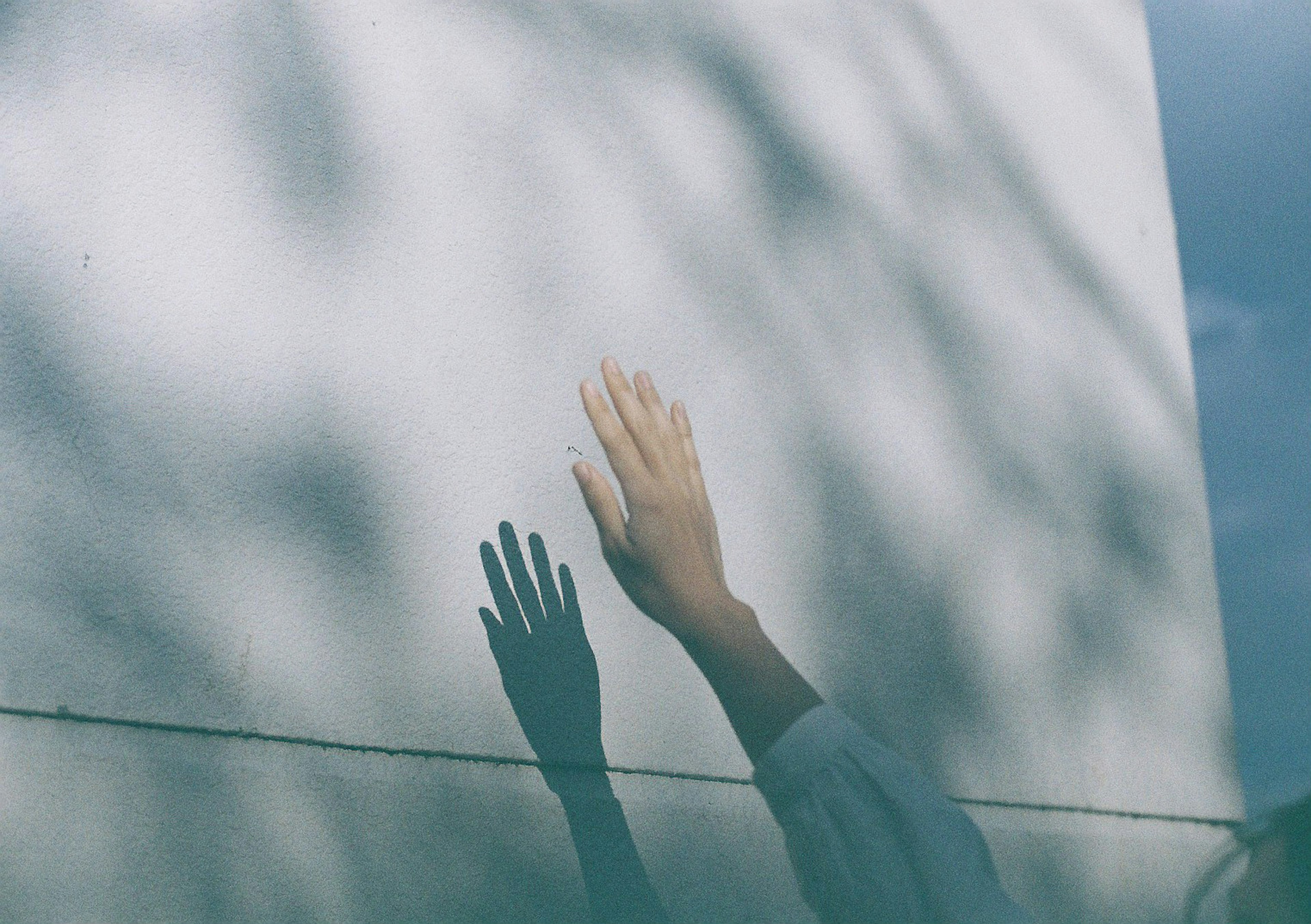 Eine Hand, die sich nach einer weißen Wand ausstreckt, mit darauf geworfenen Schatten