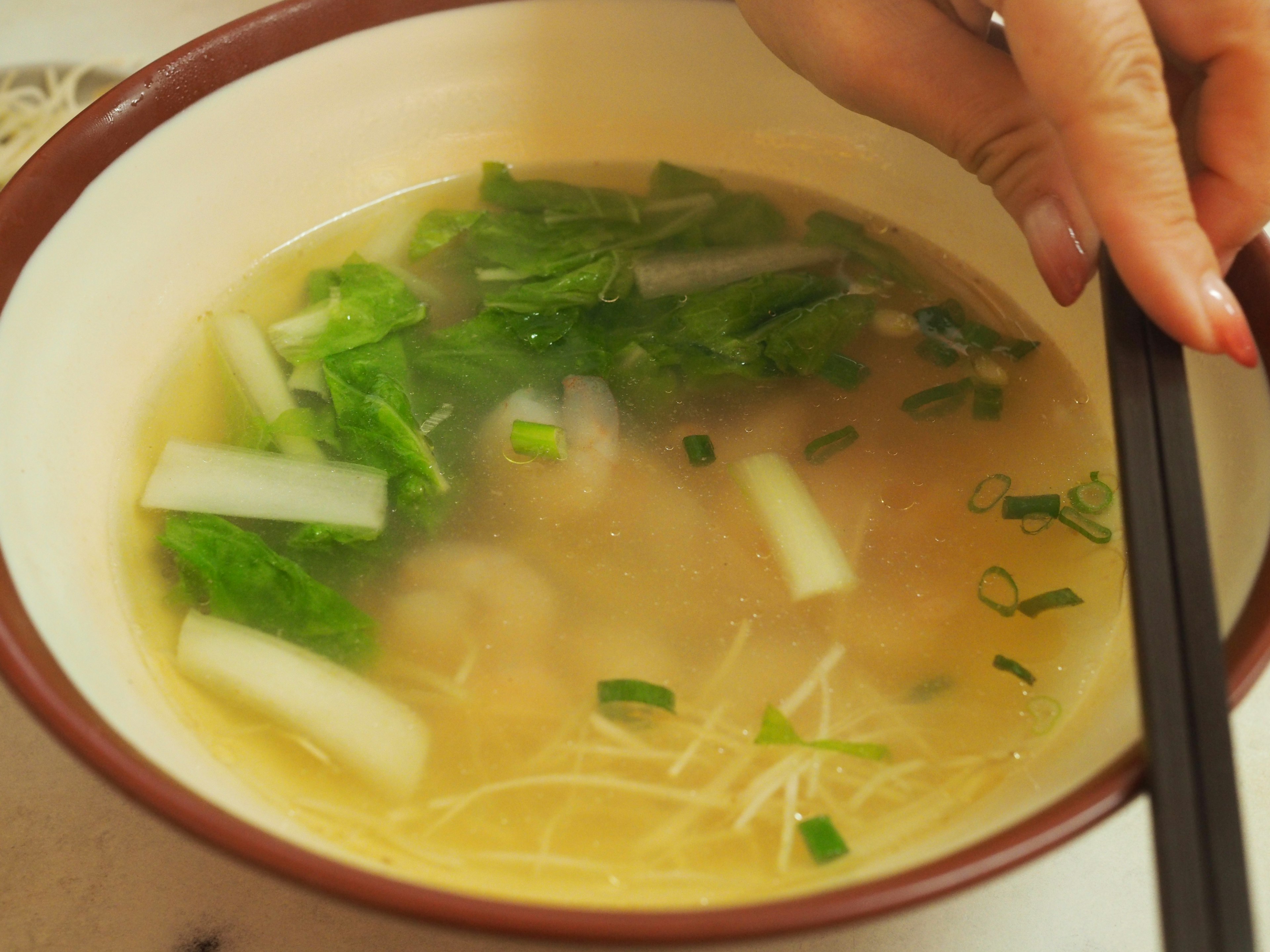 緑の野菜がトッピングされた透明なスープのボウル