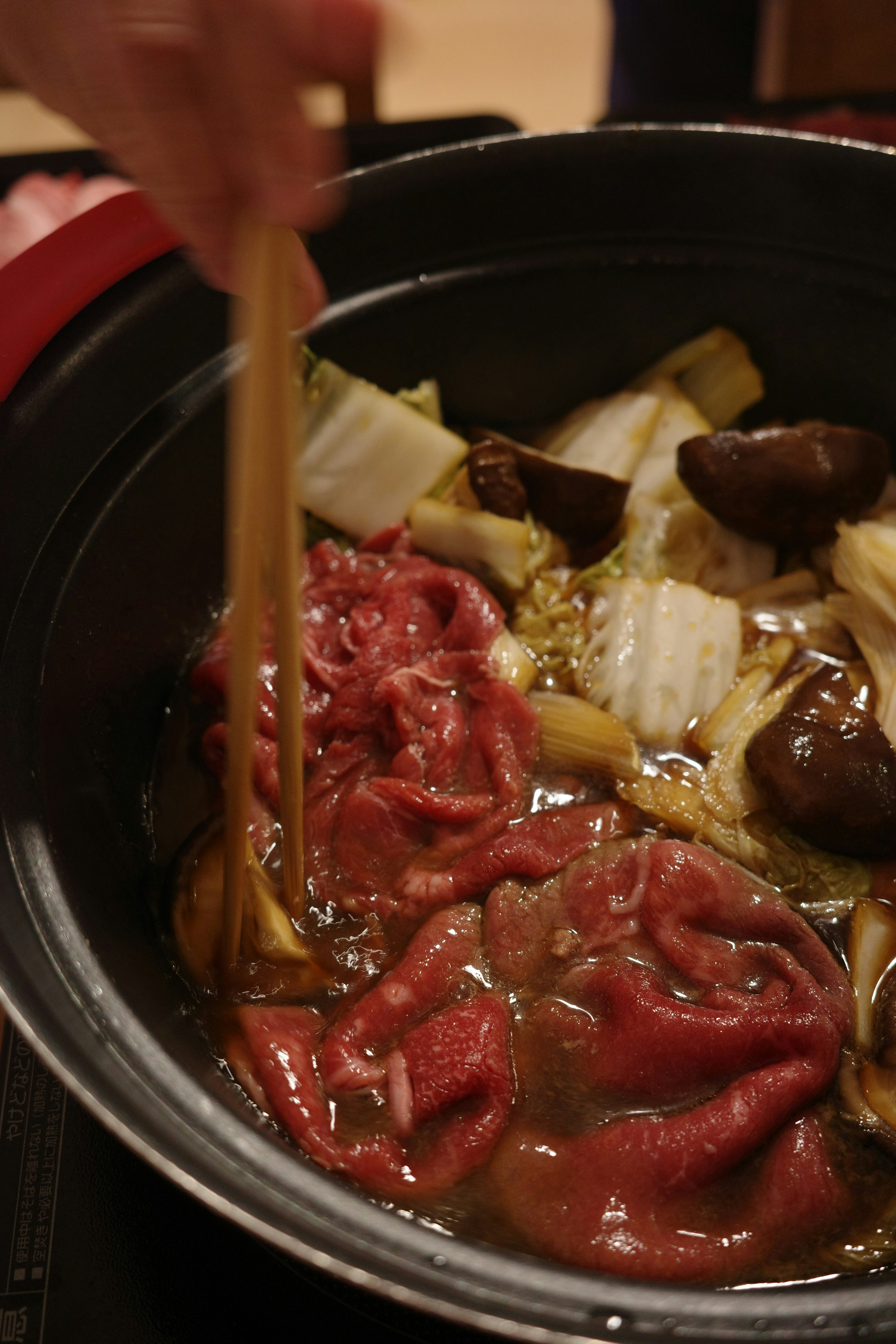 Revolviendo carne y verduras en una olla caliente con palillos