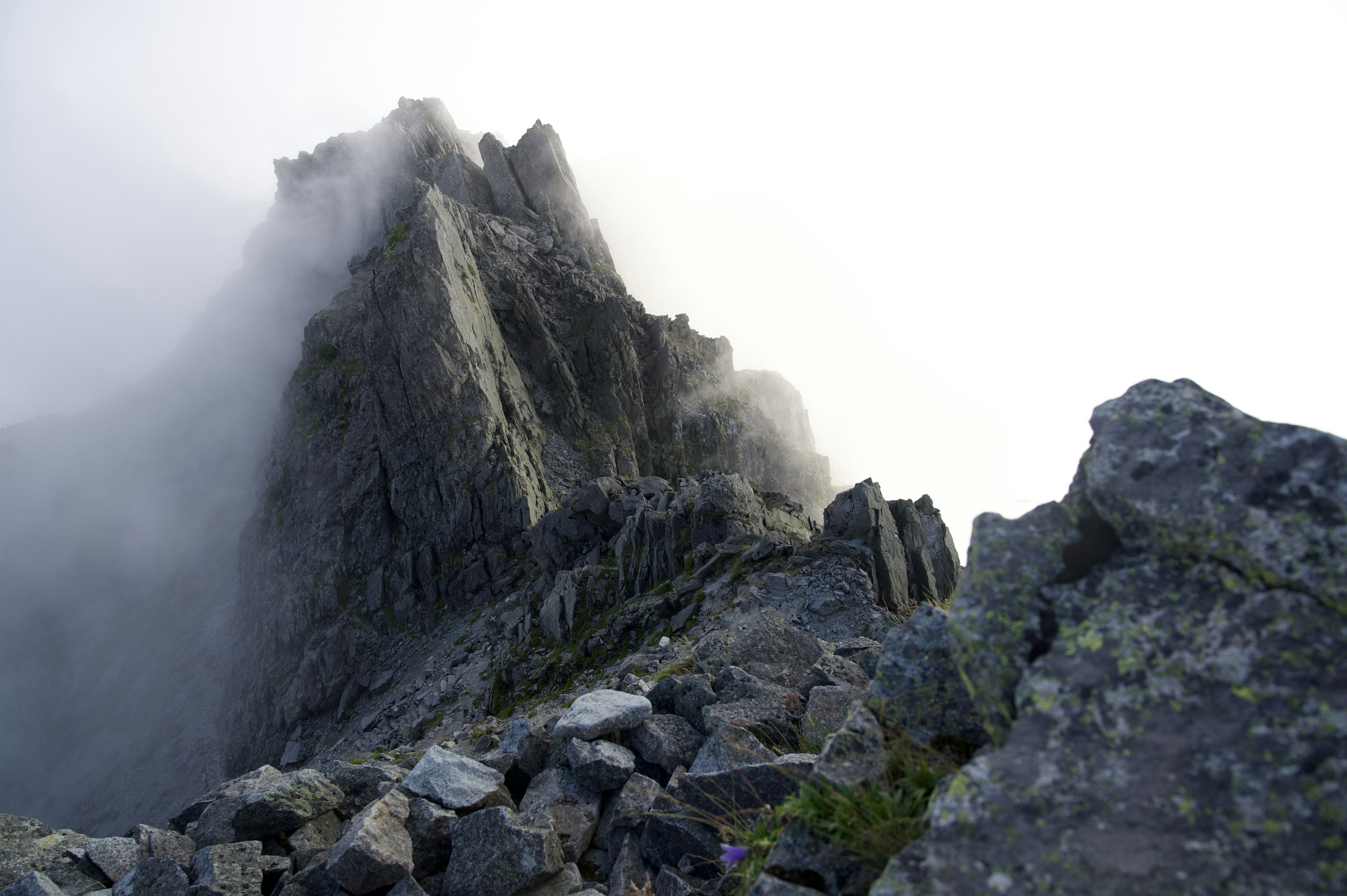 Ein zerklüfteter Berggipfel, der in Nebel gehüllt ist, mit steinigem Gelände