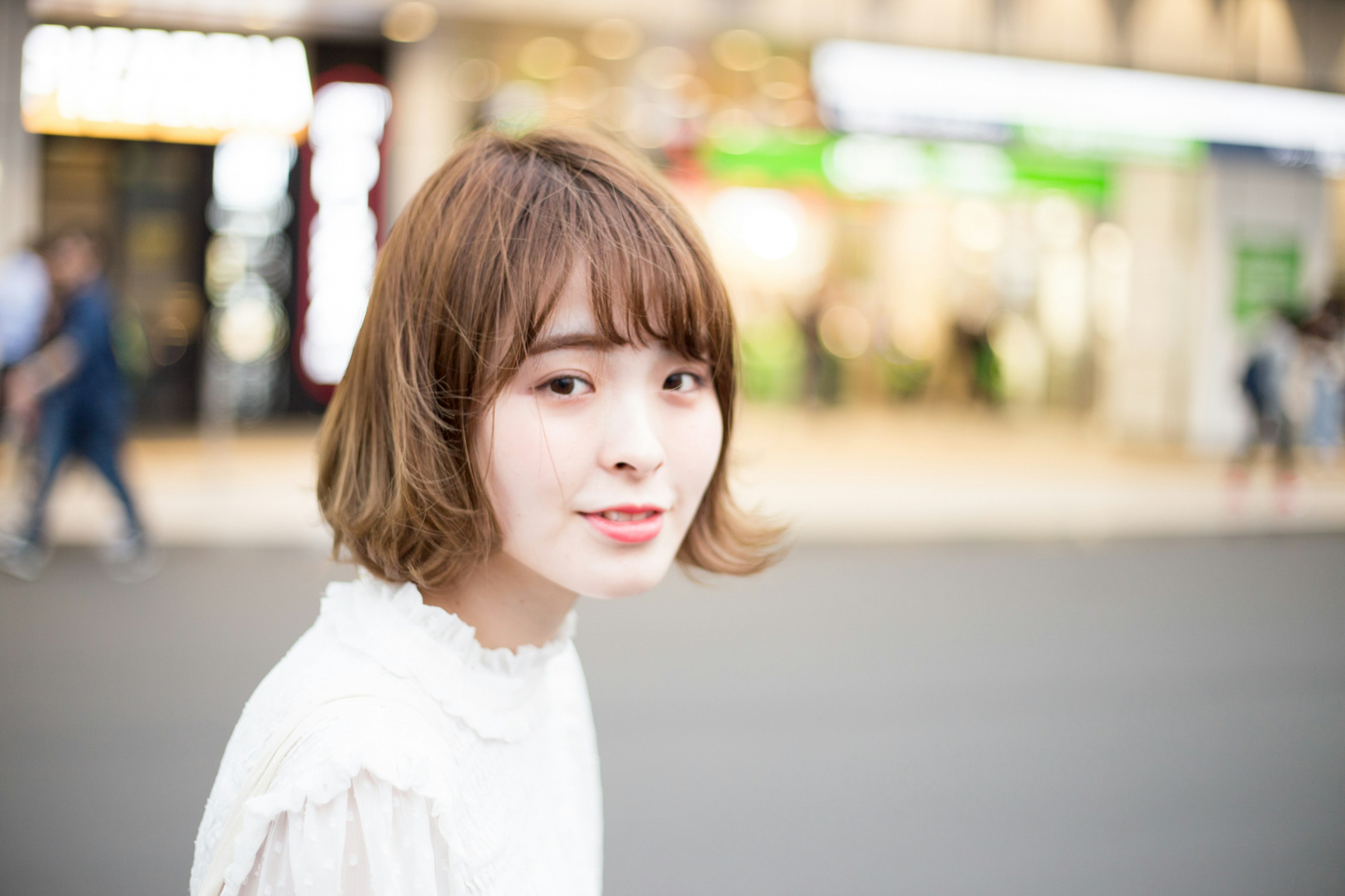 Portrait d'une femme souriante dans la rue avec une coiffure bob courte portant un haut blanc lumières commerciales floues en arrière-plan