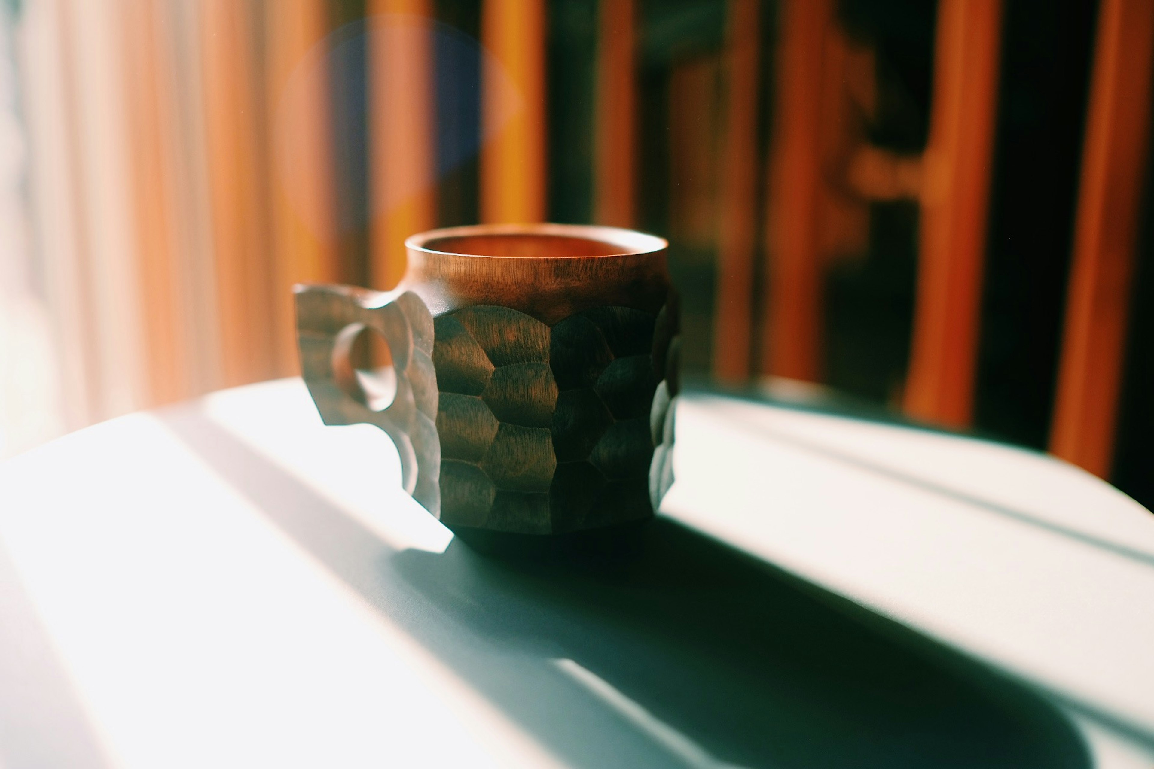 Una taza de madera colocada sobre una mesa con luz solar brillando sobre ella