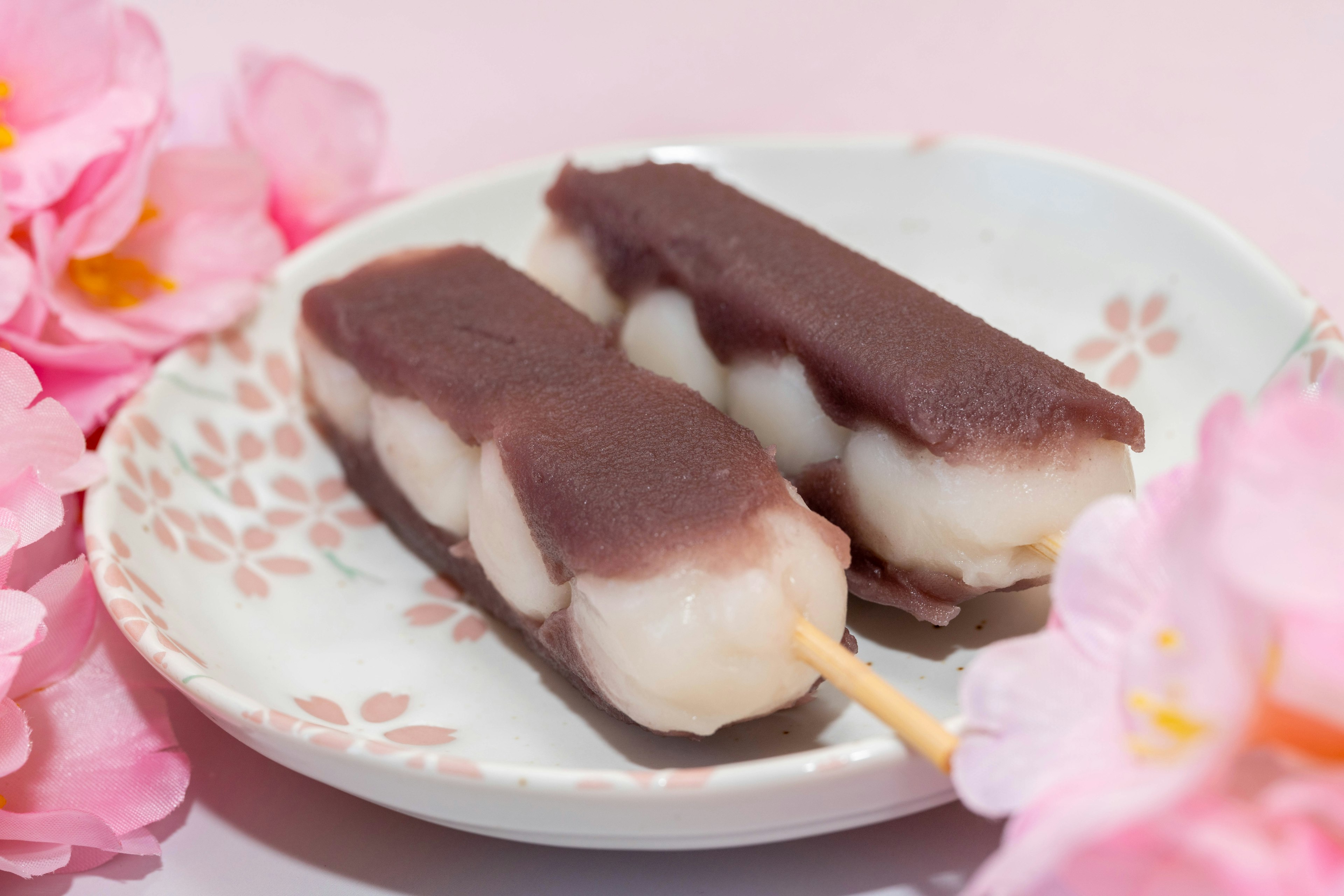 Dos piezas de dulces japoneses en un plato cerca de flores de cerezo