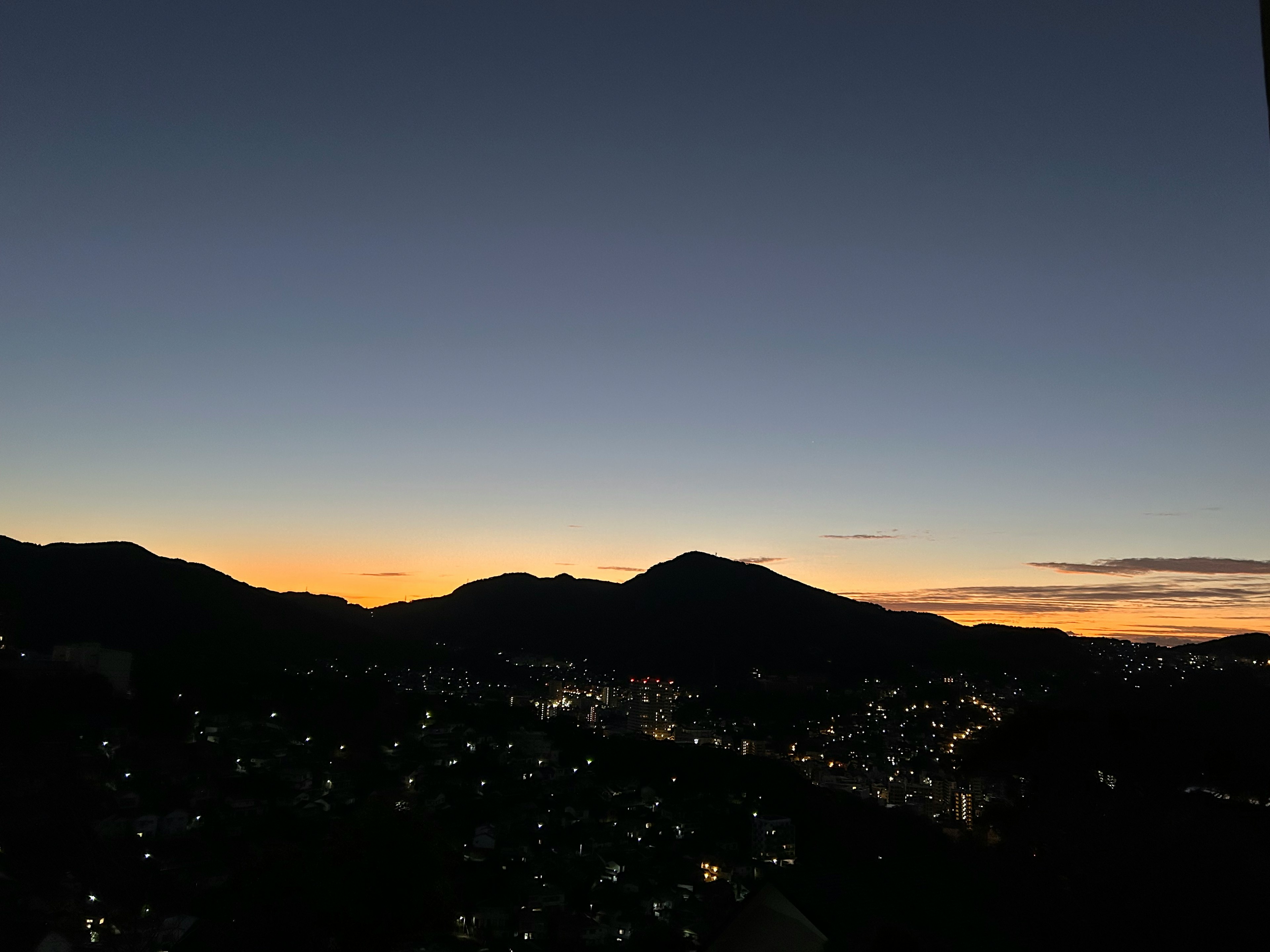 Silhouette von Bergen gegen einen Dämmerungshimmel mit Stadtlichtern