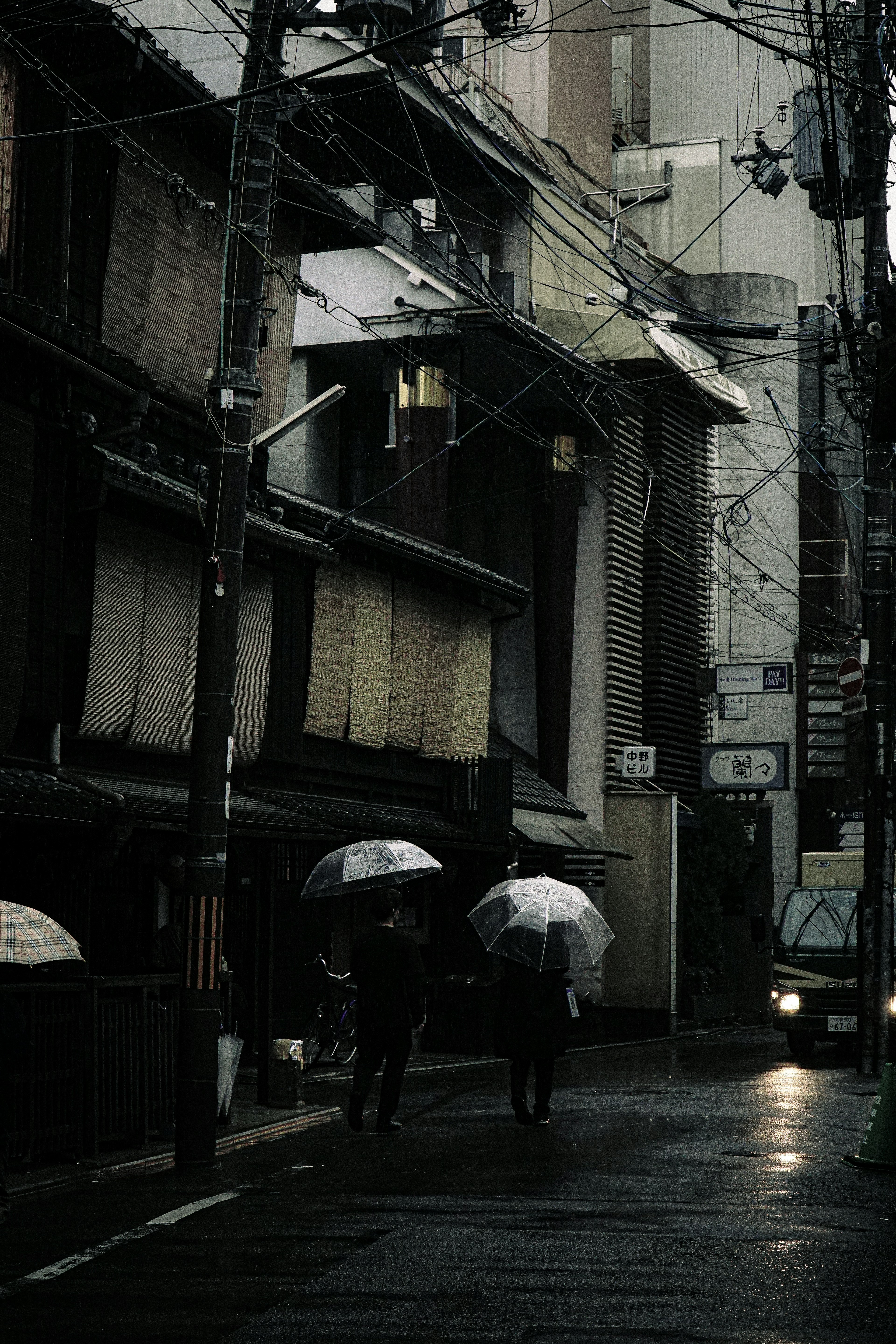 Scene of people walking with umbrellas in the rain narrow street lined with traditional buildings