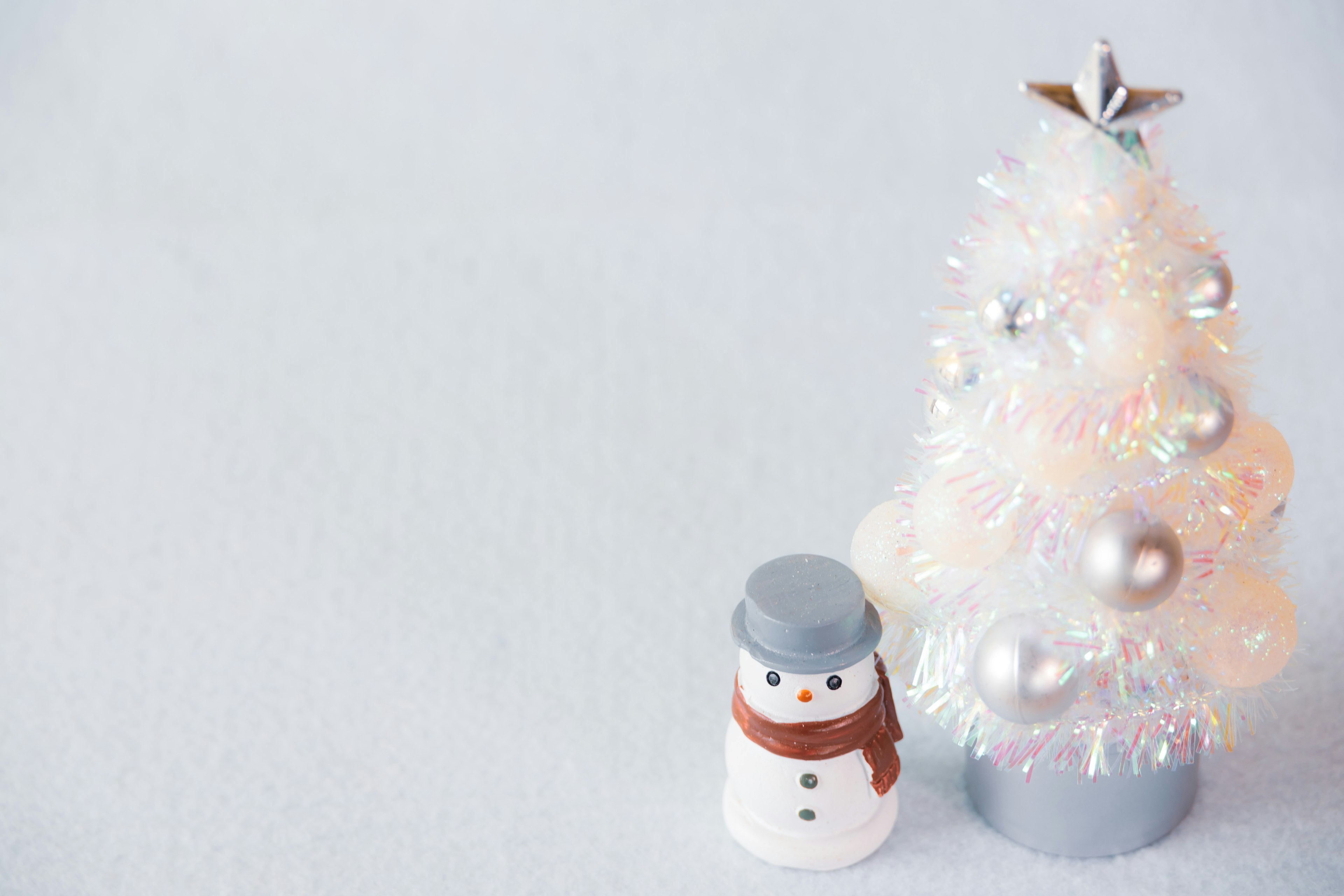 Un pequeño muñeco de nieve al lado de un árbol de Navidad blanco