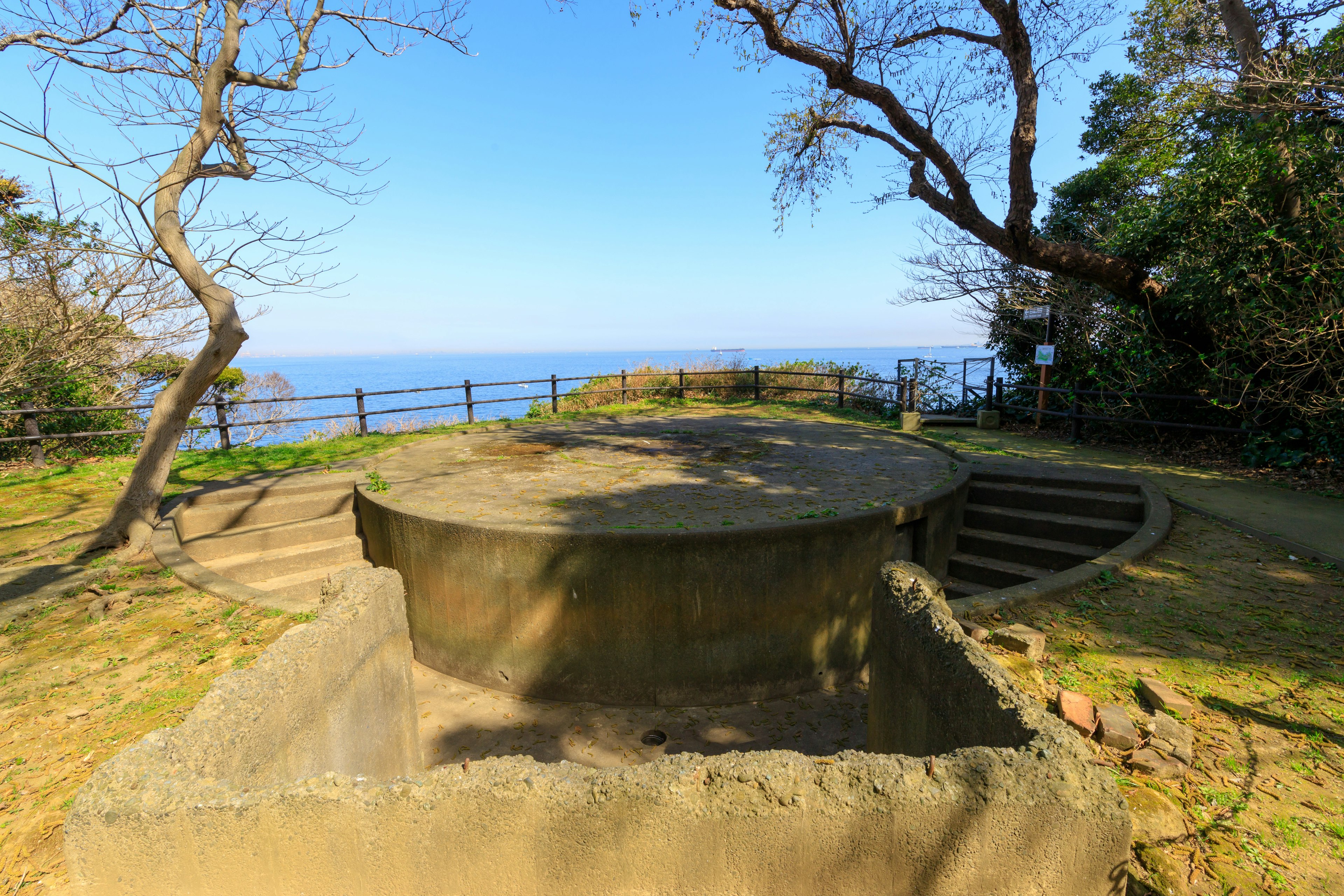 Structure circulaire en béton sur une colline verdoyante surplombant la mer