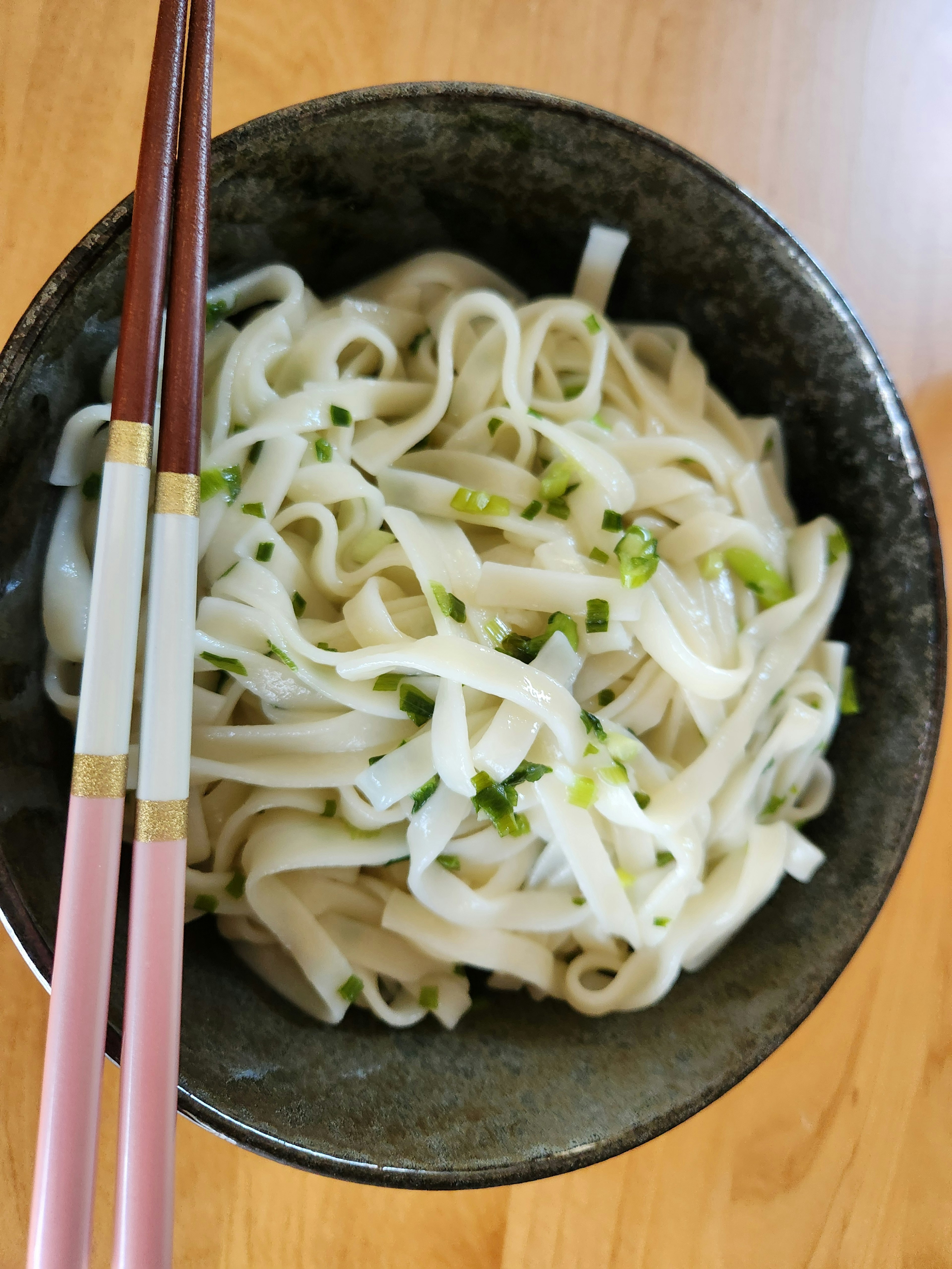 緑のトッピングを施した白い米粉の麺が盛られた黒いボウル