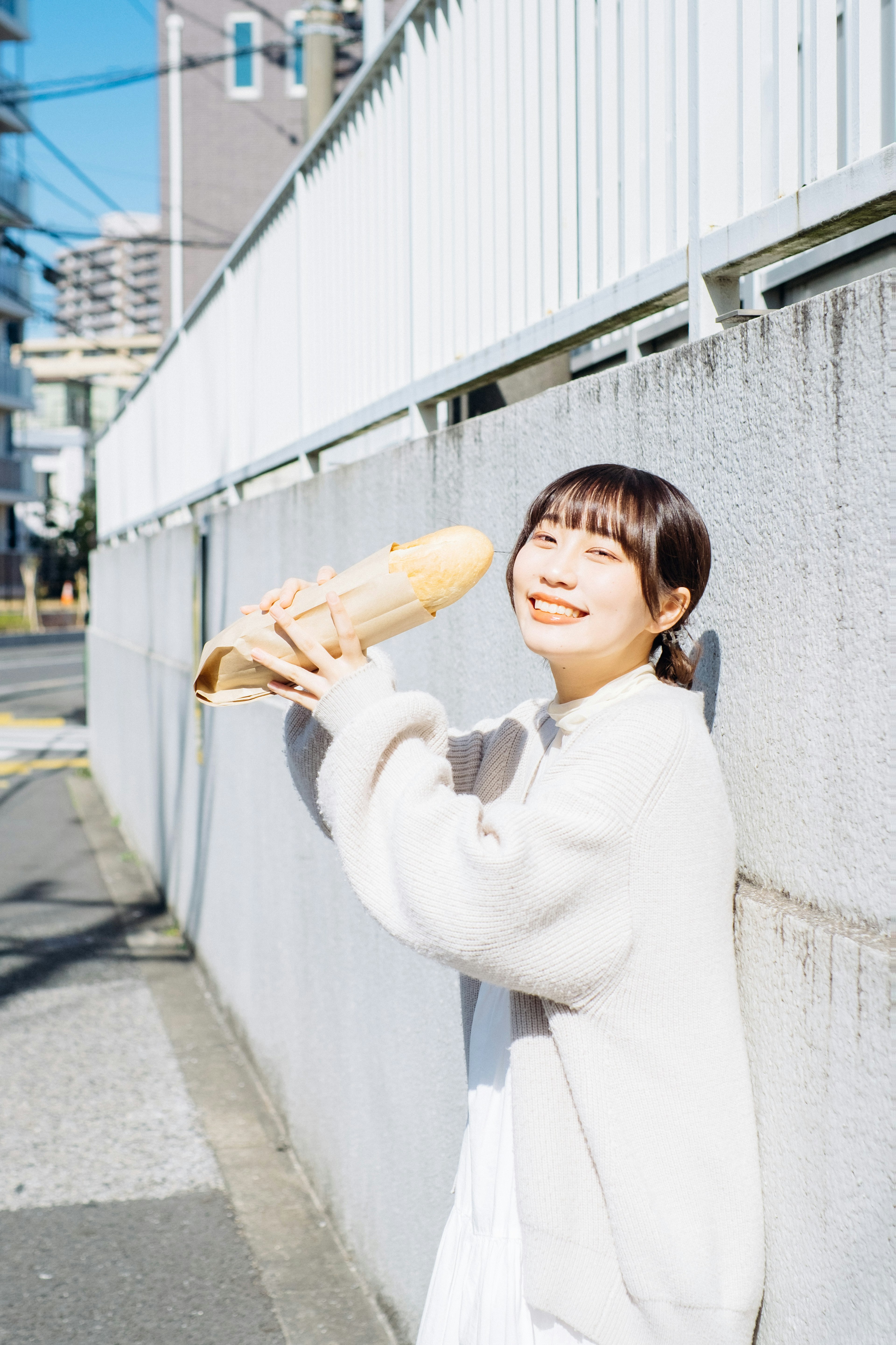 Donna in un maglione bianco sorridente mentre tiene un filone di pane