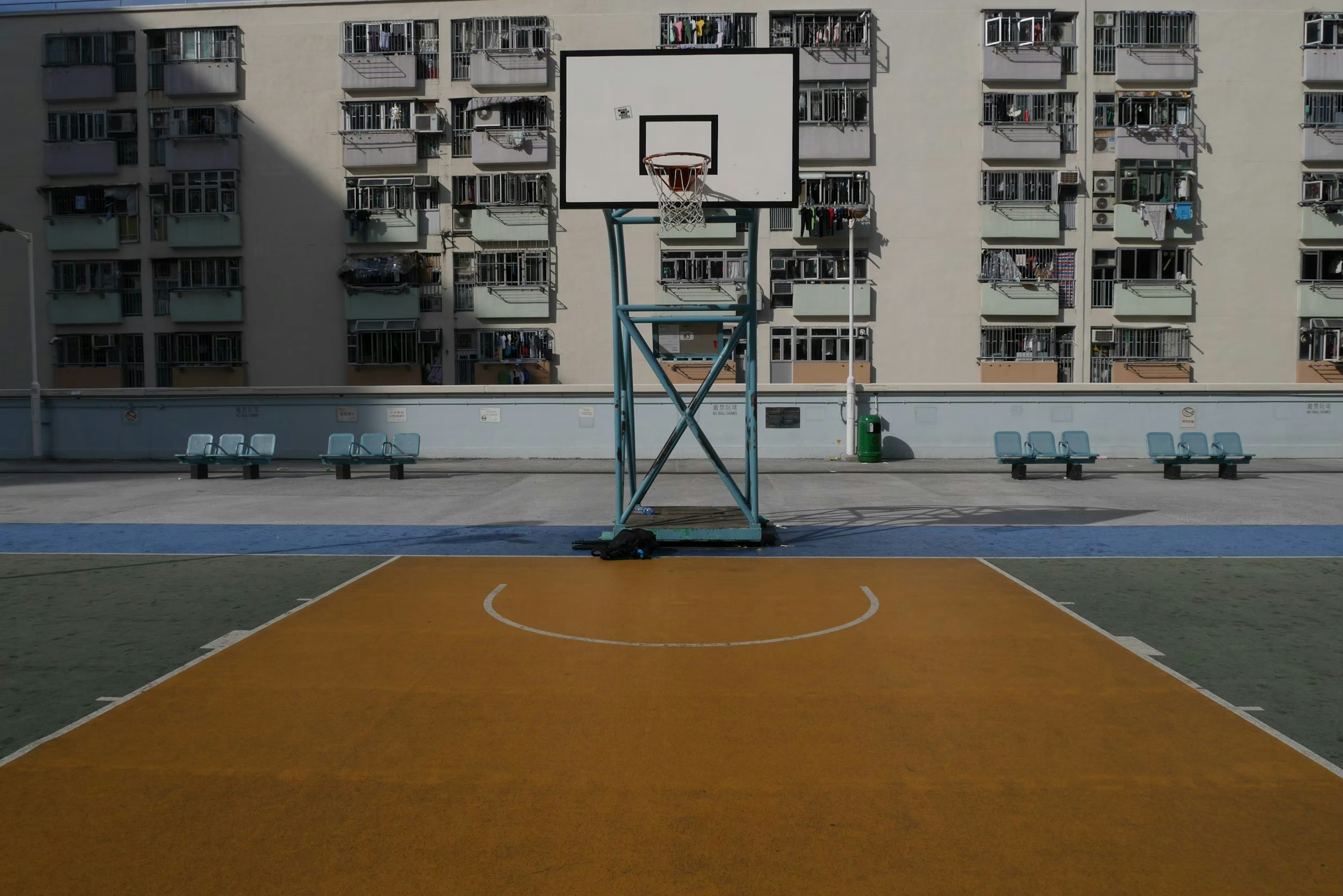 Cancha de baloncesto con un área de juego naranja y edificios residenciales al fondo