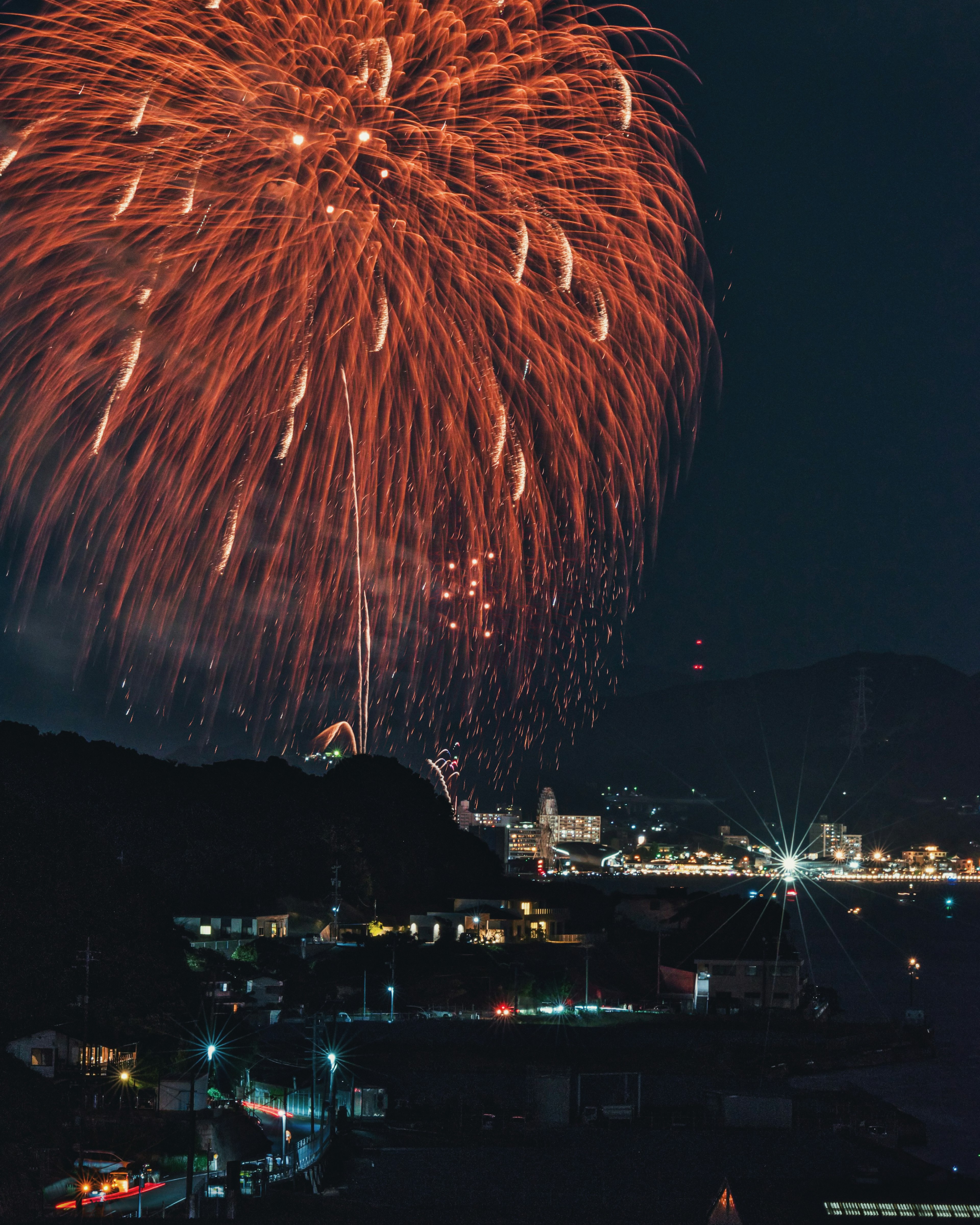 Fuegos artificiales rojos estallando en el cielo nocturno sobre un pueblo