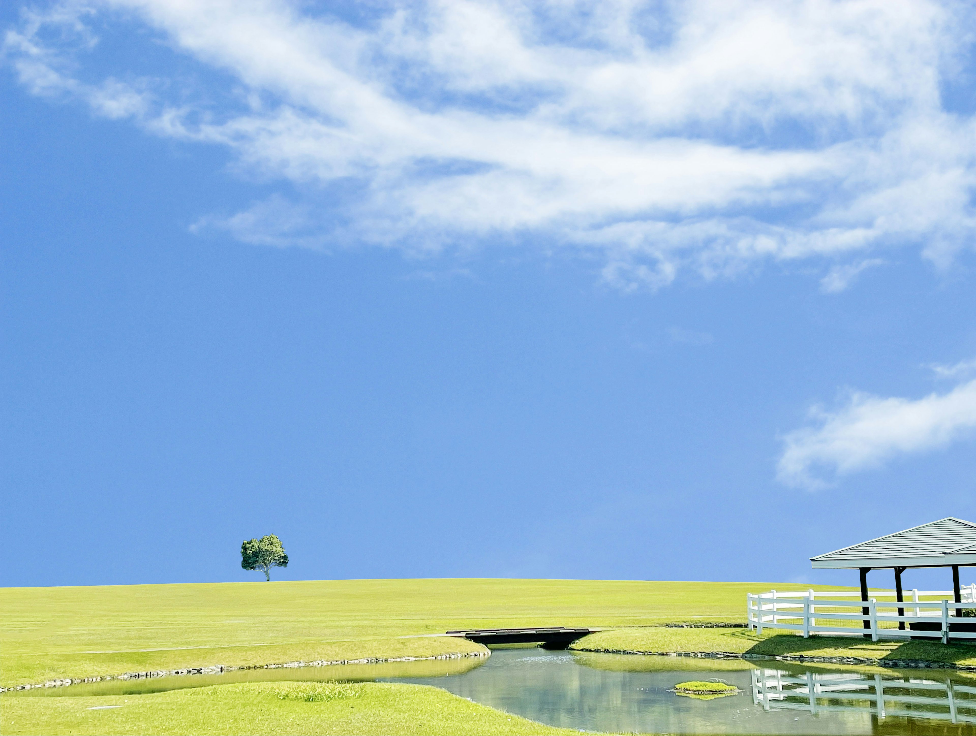 Landschaft mit grünen Hügeln und einem Teich unter blauem Himmel