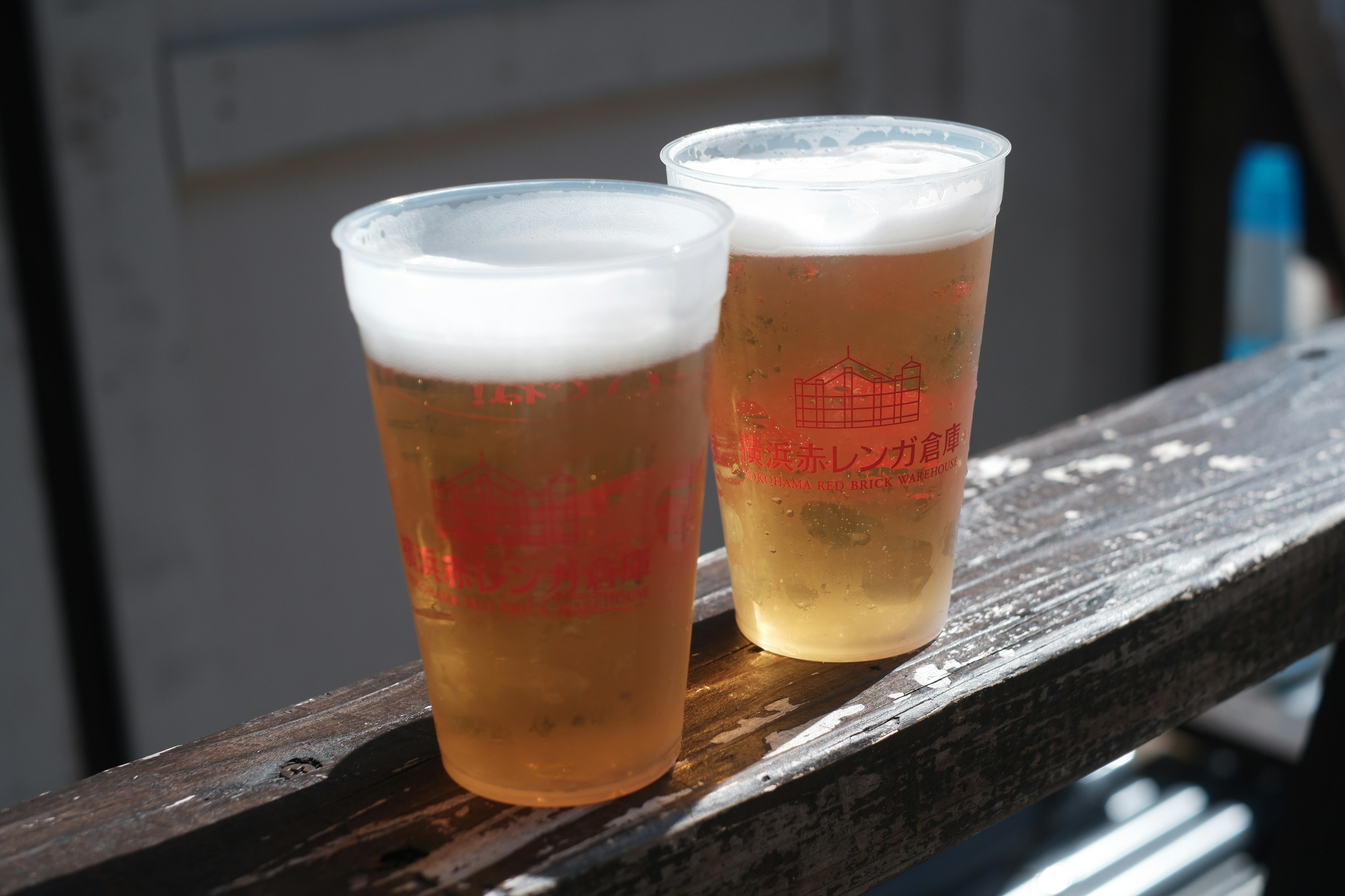 Two clear cups of beer with frothy tops on a wooden surface