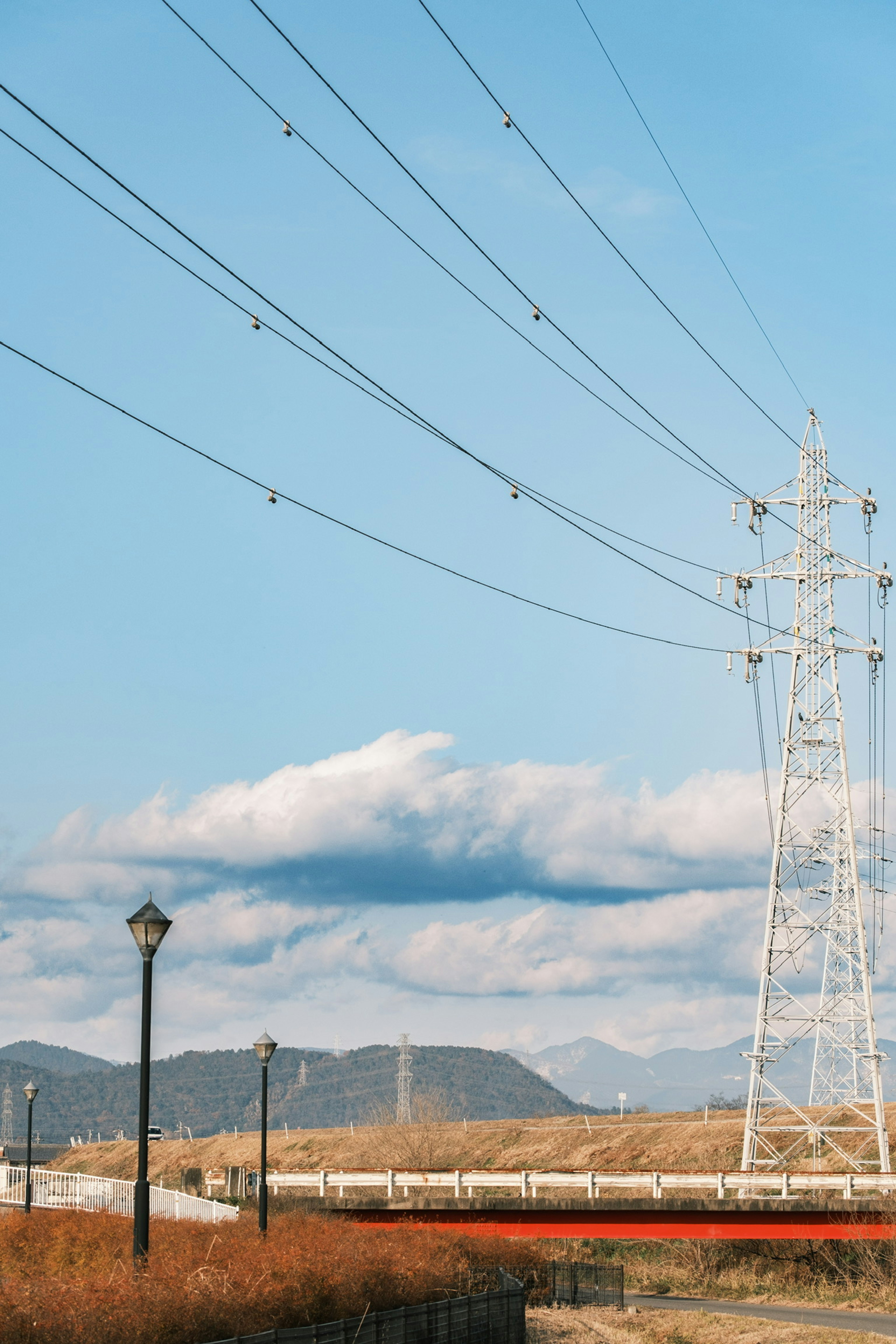 Paysage avec des lignes à haute tension et un pylône sous un ciel bleu avec des nuages