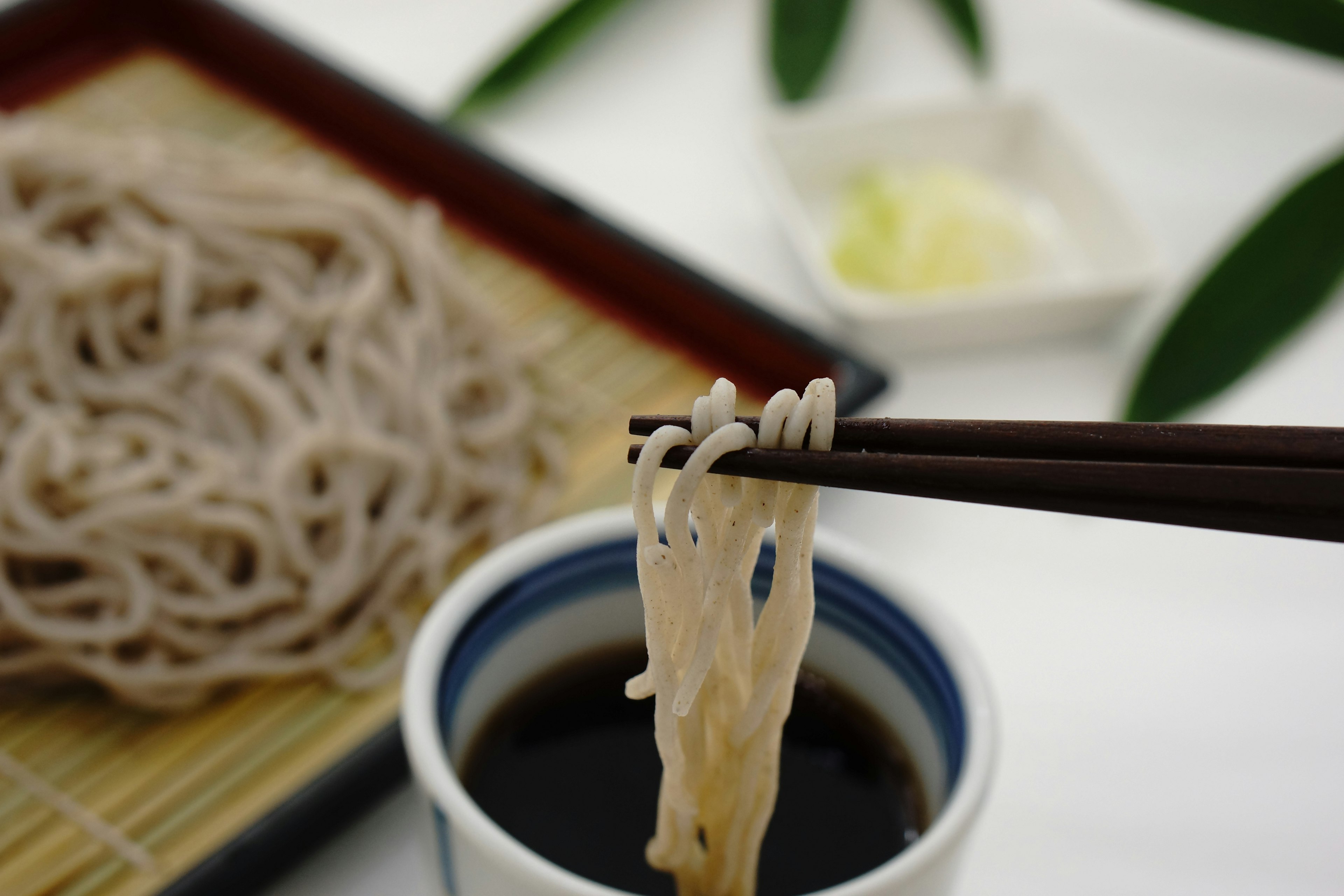 A dish of soba noodles with dipping sauce and wasabi on a bamboo mat