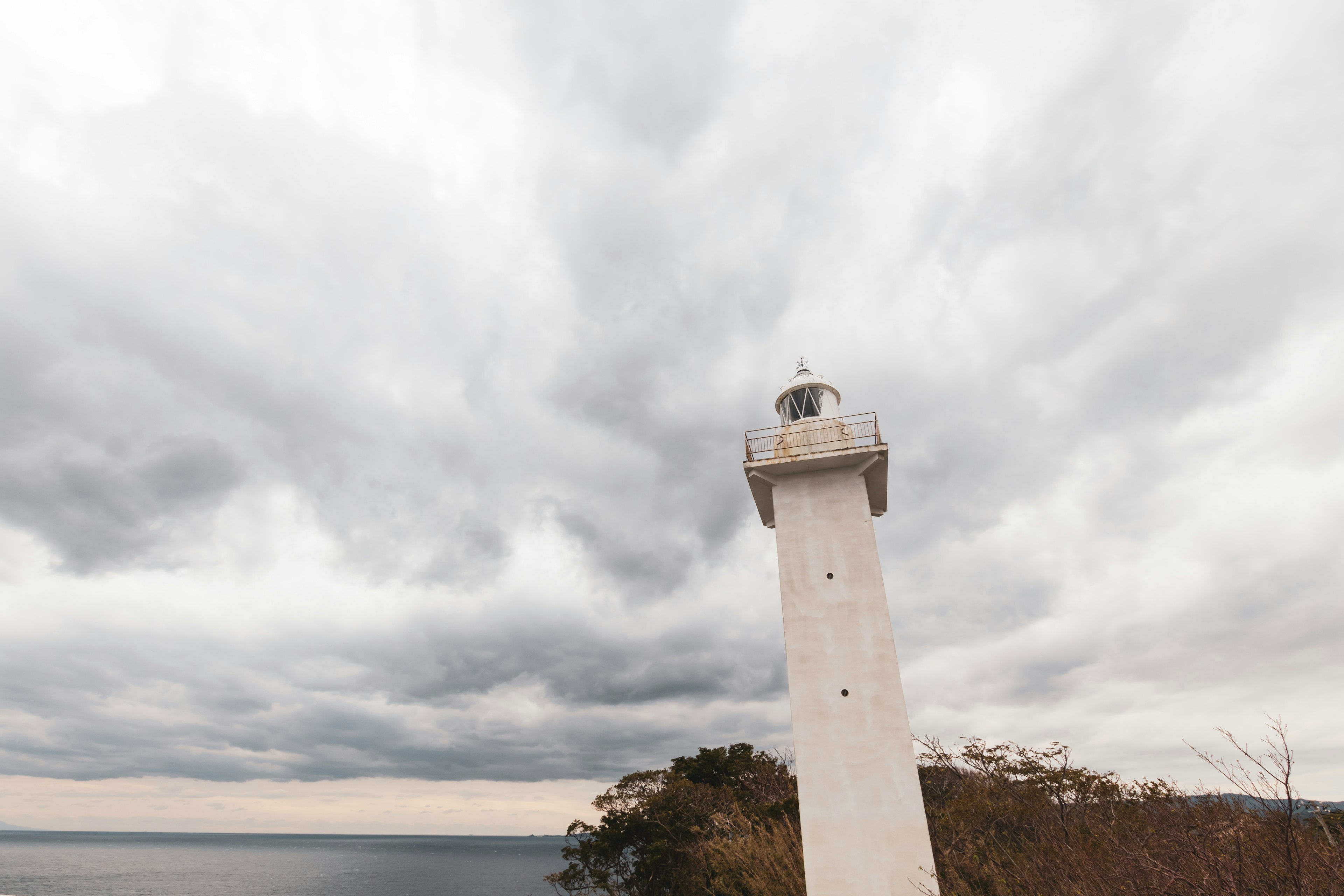 A white lighthouse standing against a cloudy sky near the coast