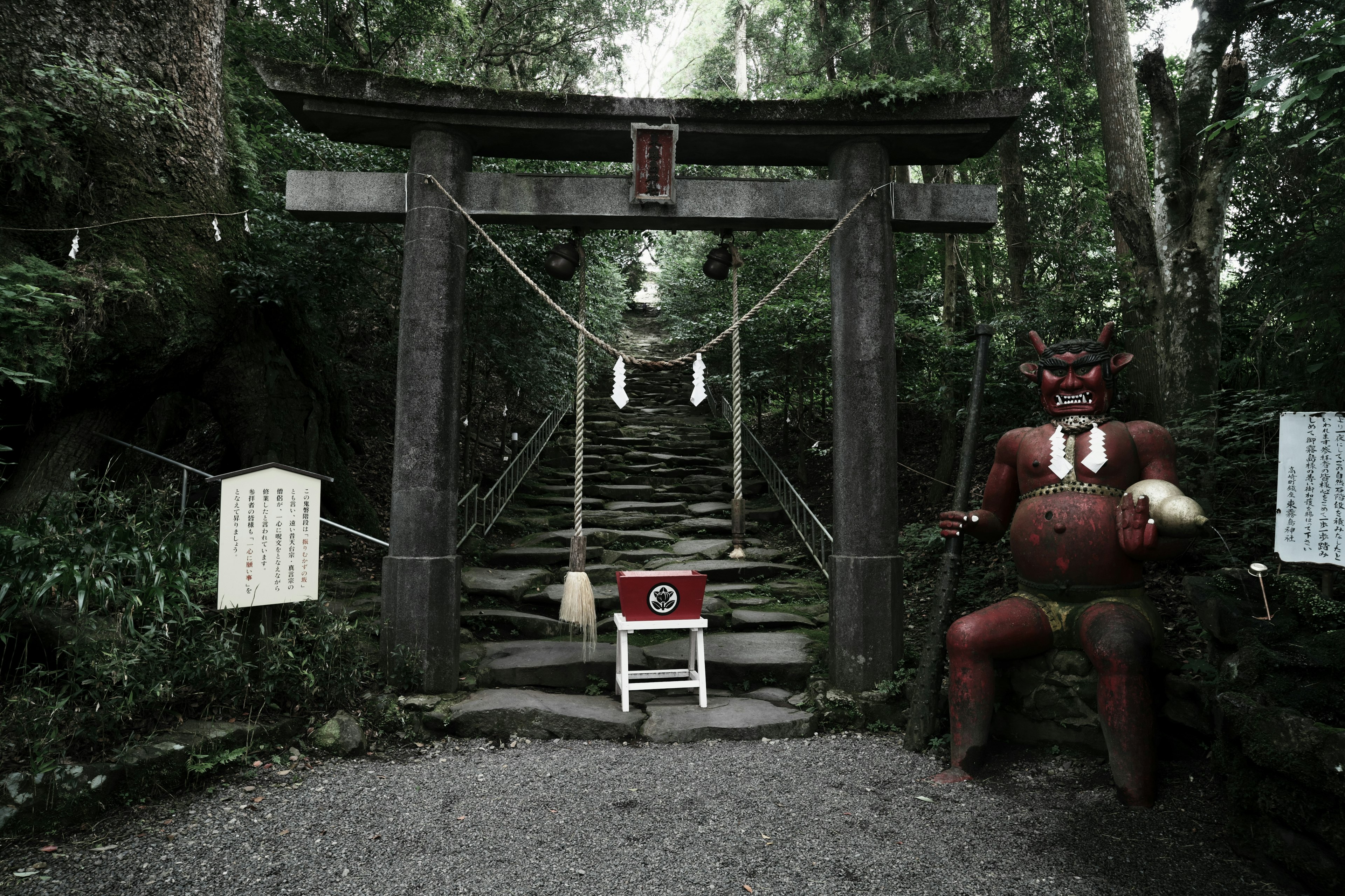 Entrada a un santuario con una estatua de demonio rojo y escalones de piedra