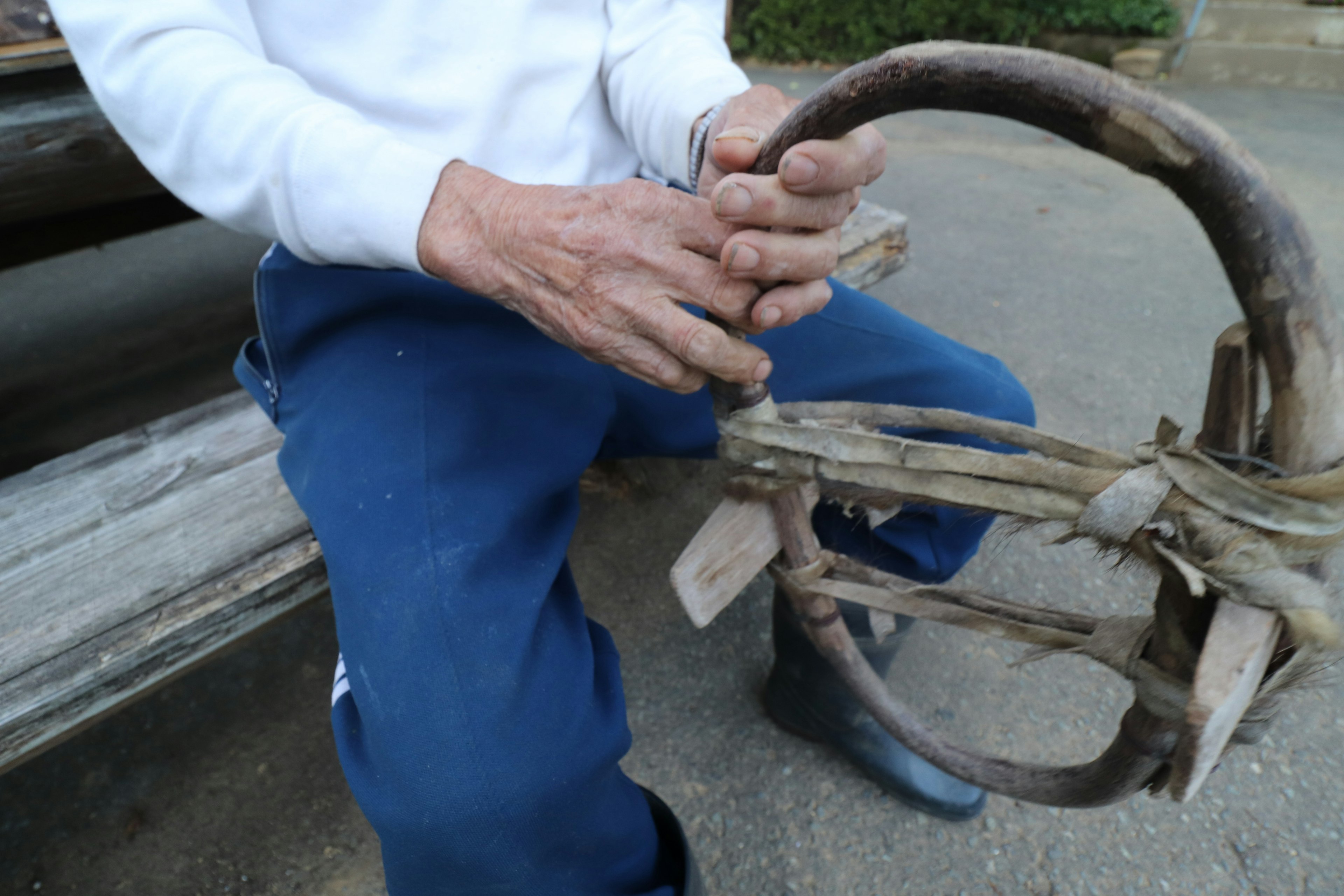 Hands of a man holding a wooden tool seated on a bench