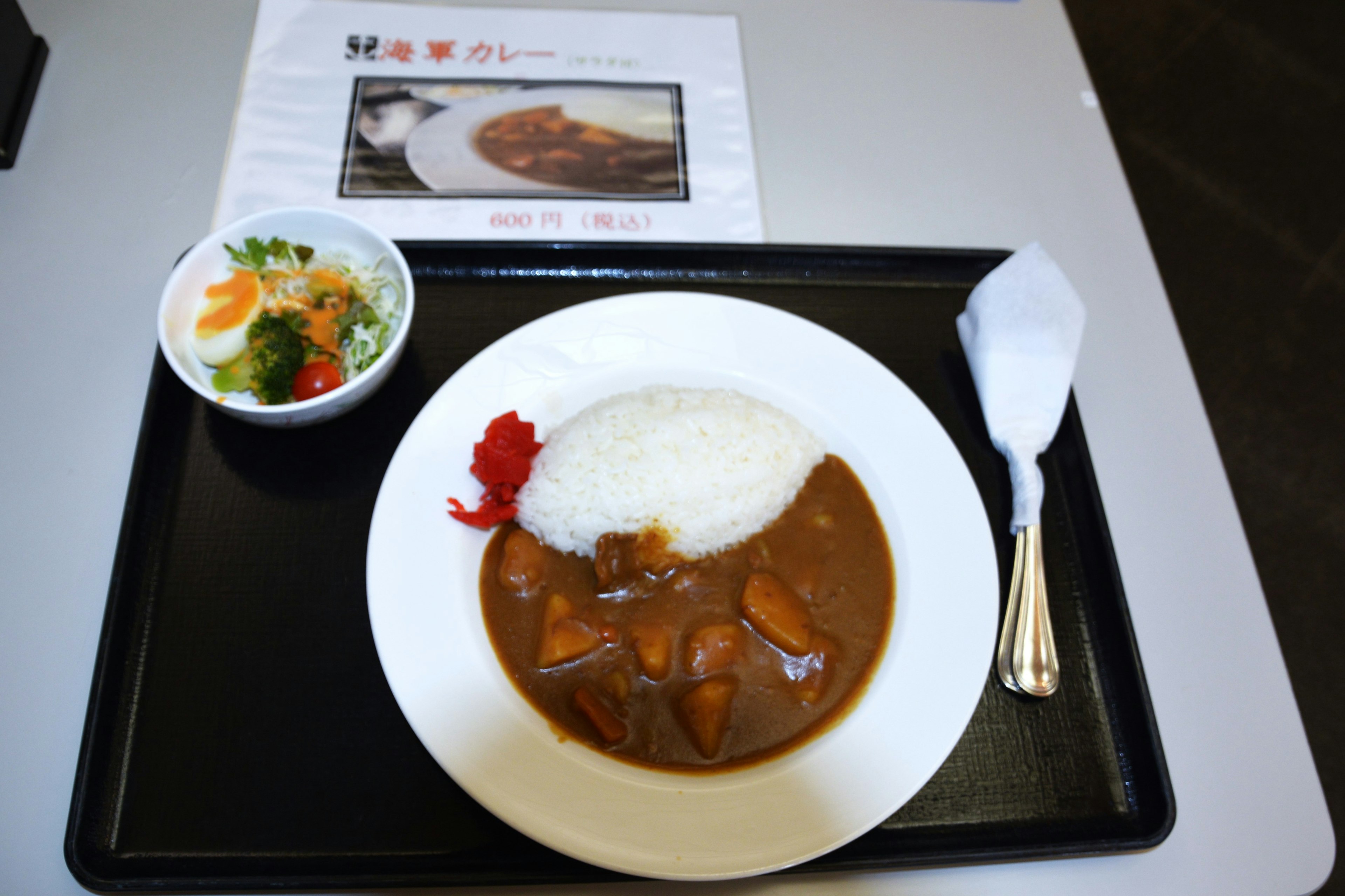 A plate of curry with rice garnished with red pickled ginger and a side salad