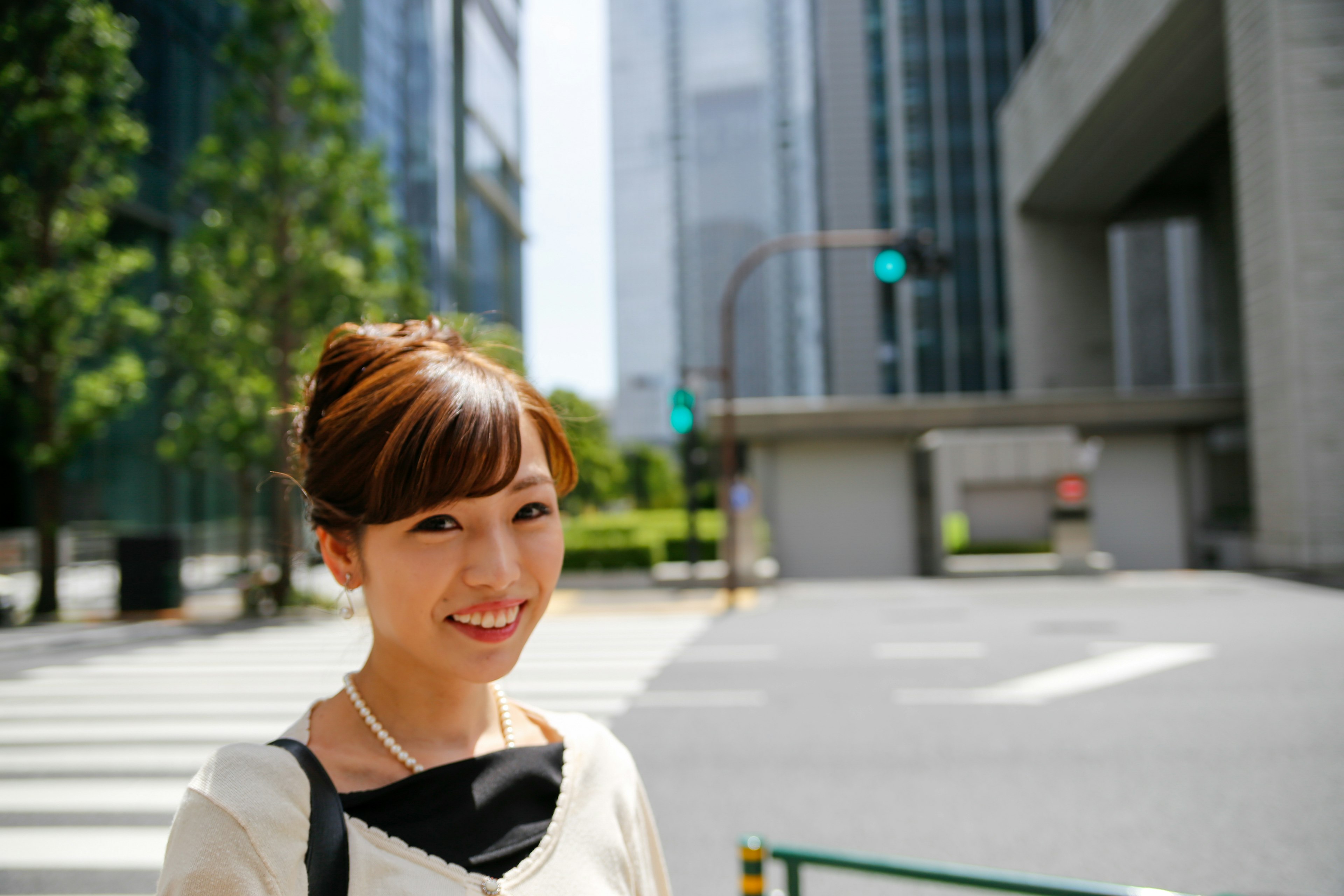 都会の風景に立つ女性 笑顔の近景 緑の木々と高層ビルが背景