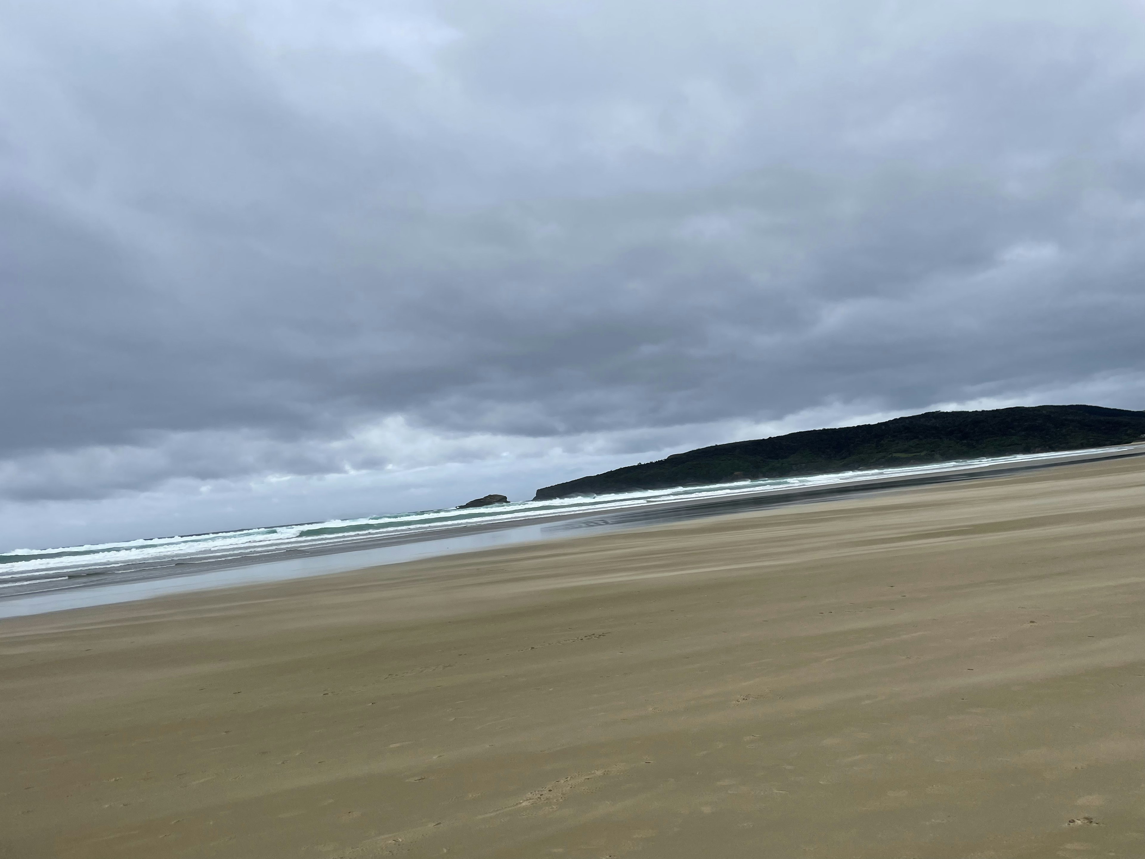 Escena costera con nubes grises sobre una playa de arena olas suaves rompiendo en la orilla